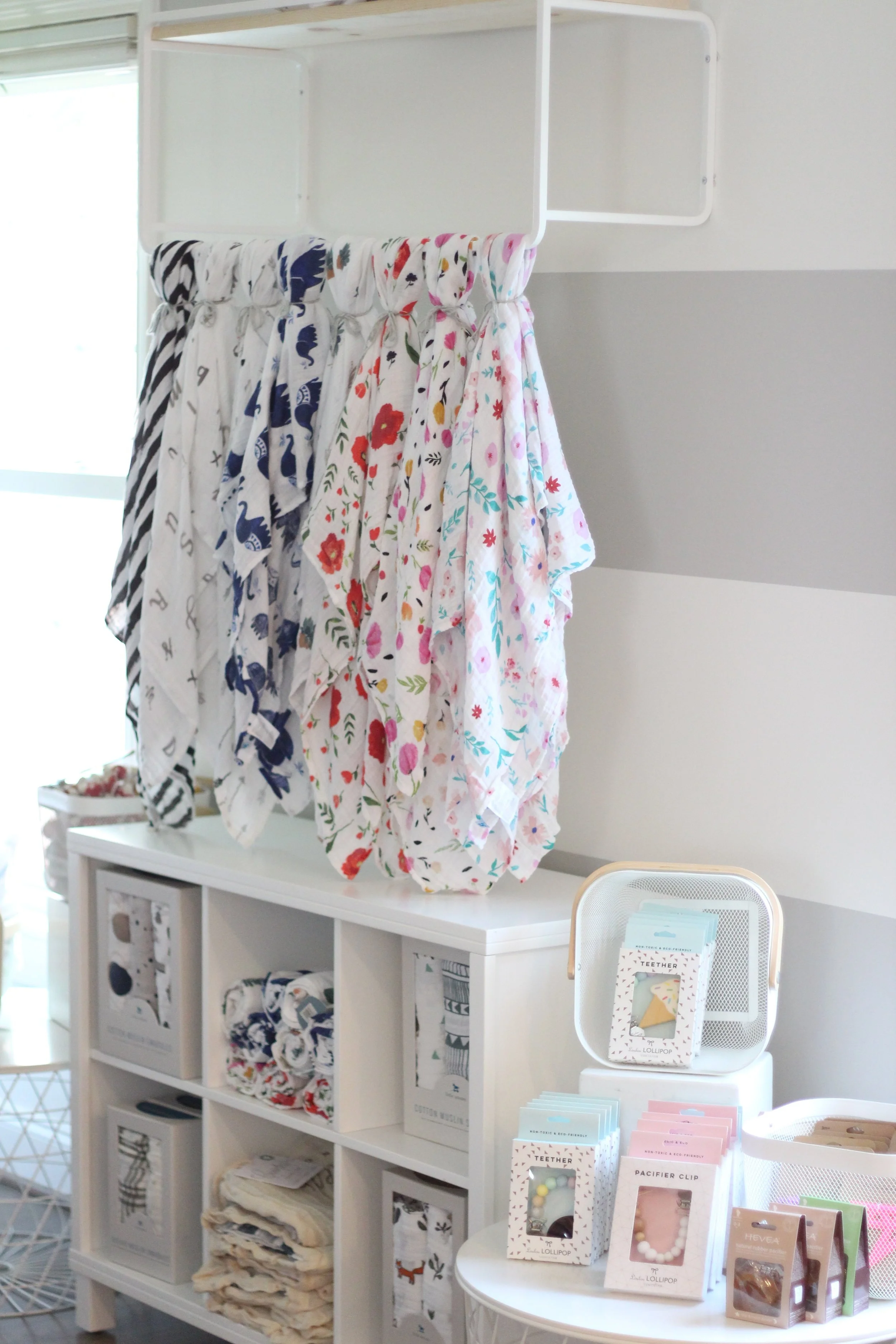 Display shelf with folded textile items, hanging fabric pieces with animal and floral prints, and shaped accessories on a round table.