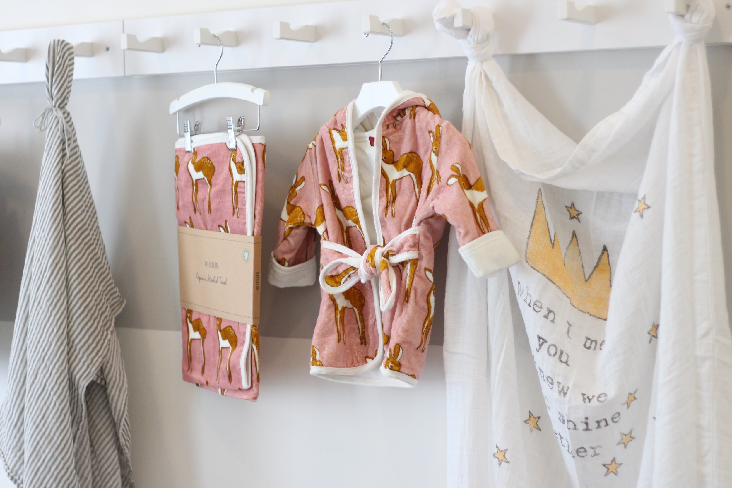 Children's pajamas with a horse pattern hanging on a hook in a dressing room, alongside other clothing and a decorative white cloth with stars.