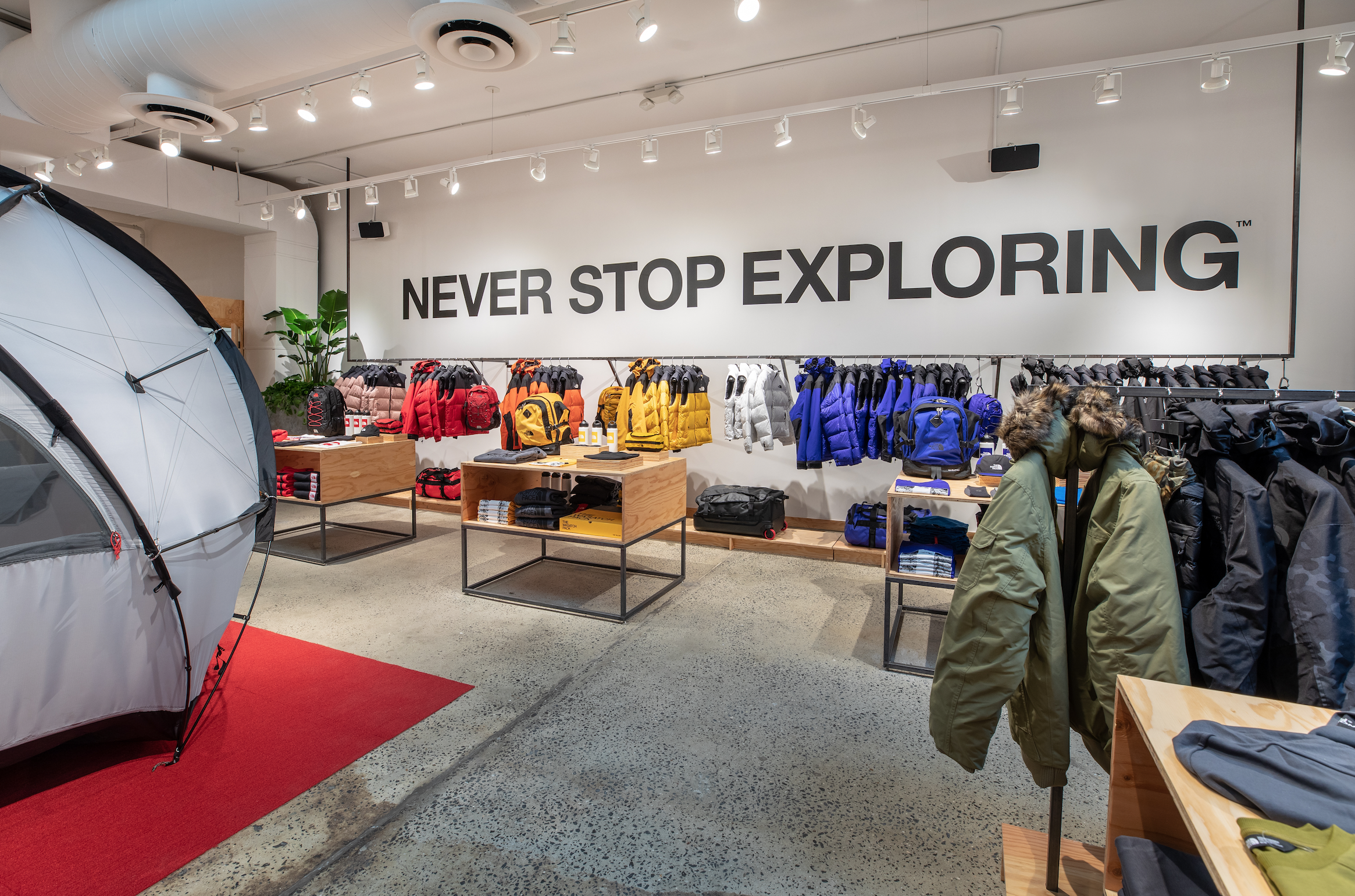 Display of outdoor jackets and backpacks inside a retail store with a large sign that says, 'Never Stop Exploring.'