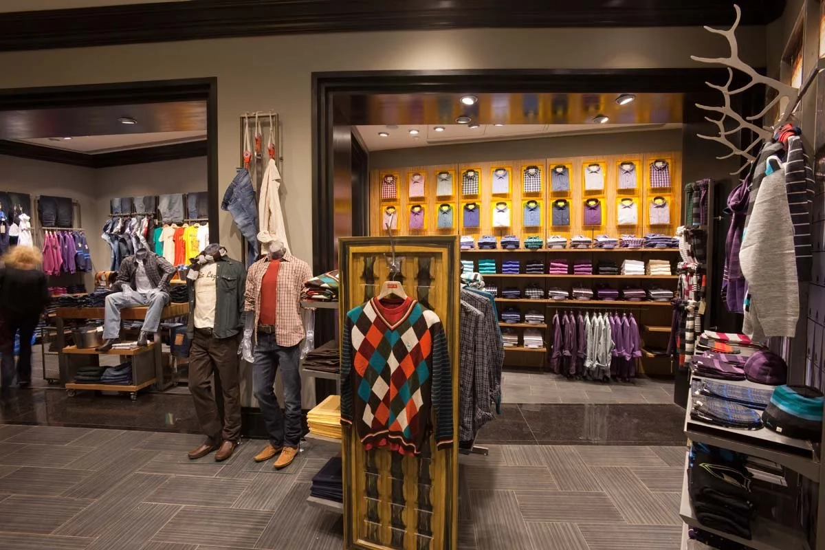 Clothing store displays with mannequins, shelves of shirts, folded clothes, and jackets arranged on racks and walls.