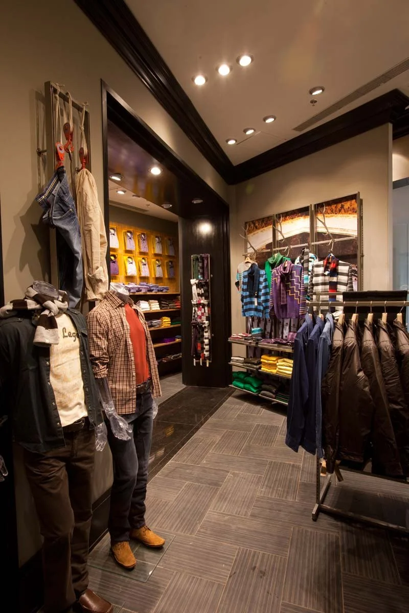 Interior of a men's clothing store with mannequins dressed in casual outfits, shelves with folded shirts, and colorful striped sweaters on display.