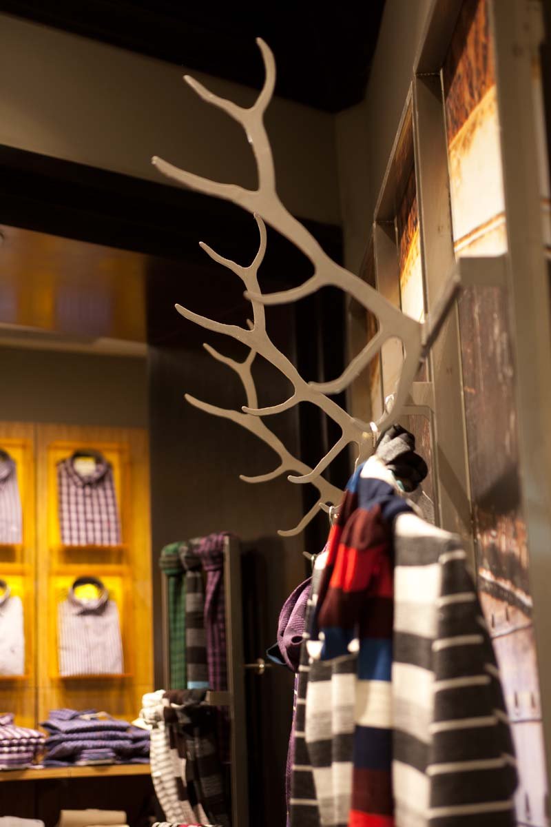 A store display with a white, branch-shaped coat rack holding striped and checkered shirts, with folded clothing on shelves behind.
