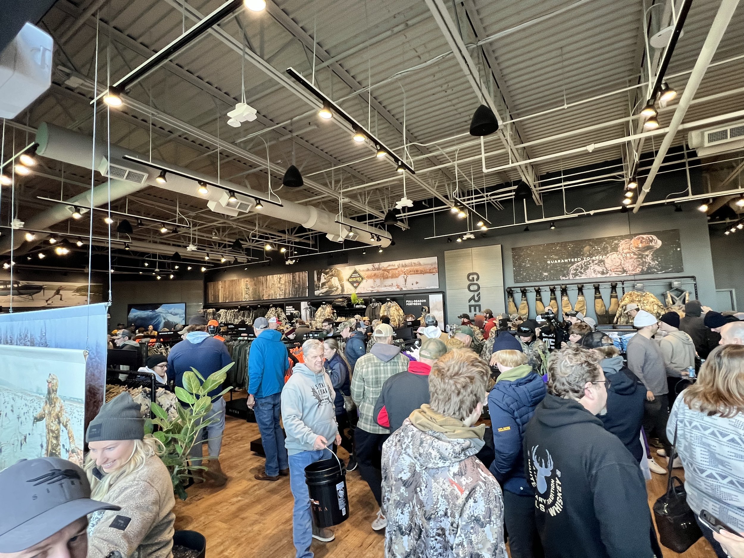 Crowd of people shopping in an outdoor gear and hunting equipment store with camouflage clothing and gear on display.