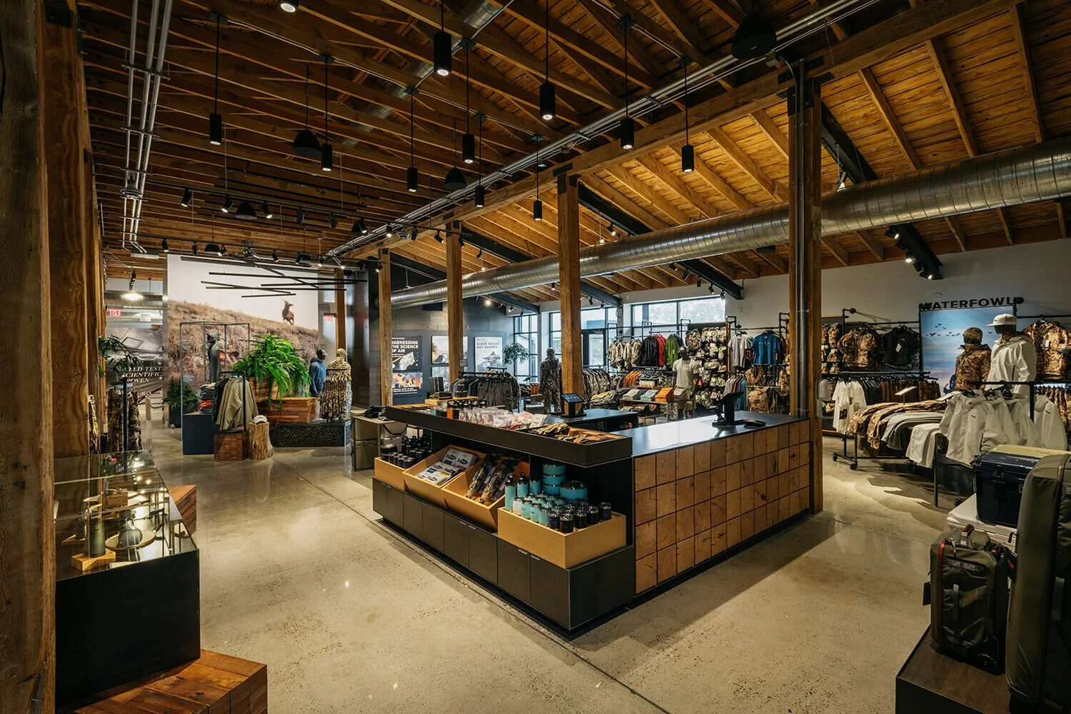 Interior of an apparel store with clothing displays, mannequins, and decorative elements, featuring a rustic wooden ceiling and industrial ducts.