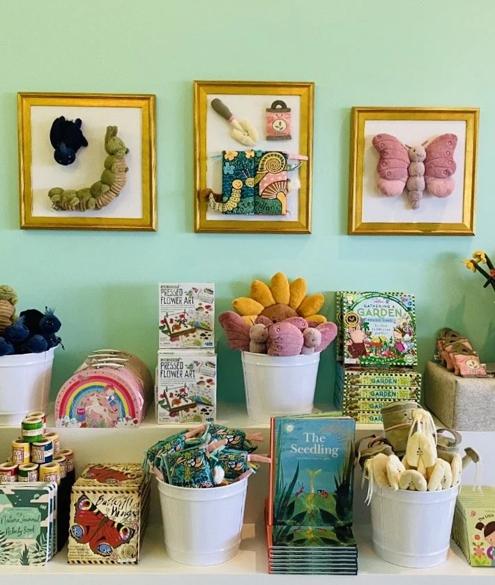 Display of children's toys, books, and plush animals arranged on a table in a toy or gift shop with pastel-colored walls.