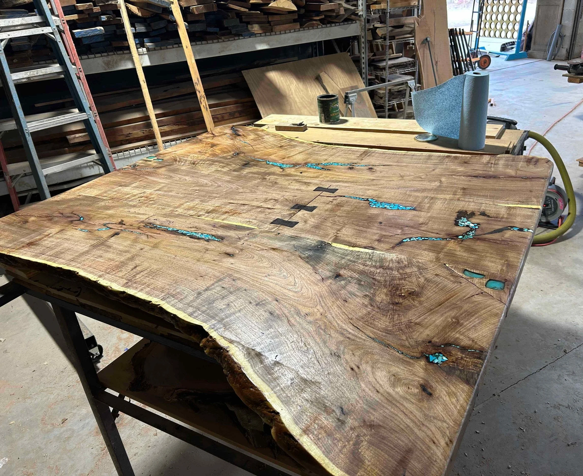A large, live edge wood tabletop with inlay work on a work table in a workshop.