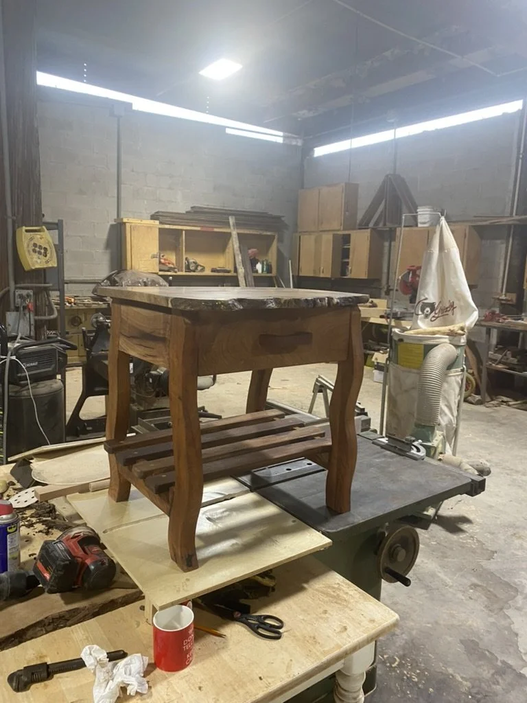 A wooden side table with a lower shelf in a woodworking shop.