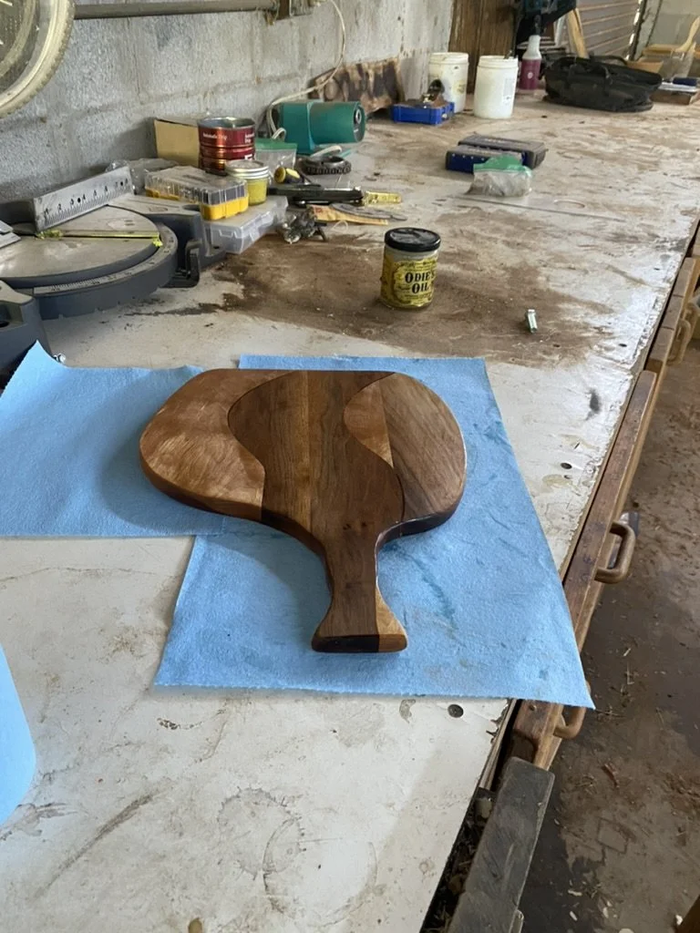 A wooden paddle-shaped cutting board on a blue cloth on a workshop workbench.