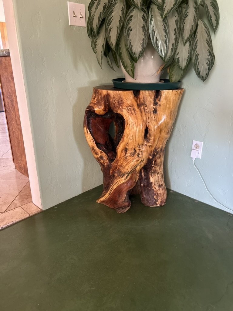 A wooden tree stump used as a plant stand with a potted plant on top of it, placed against a green wall.