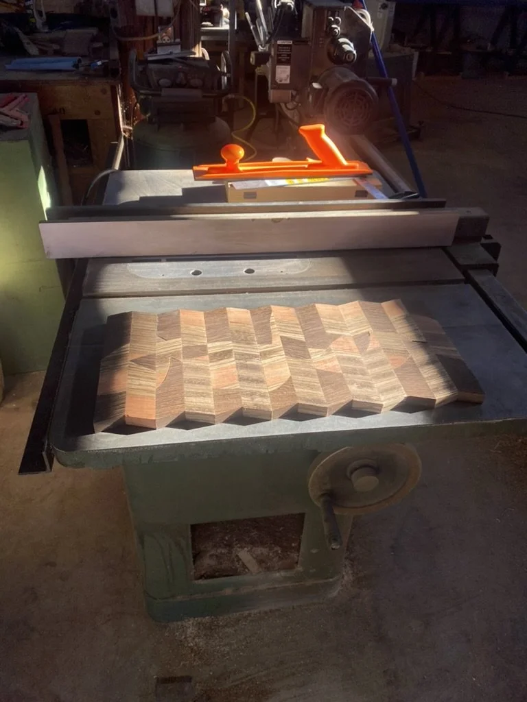 A woodworking table saw with a partially cut geometric patterned wooden piece on the surface, in a workshop setting.