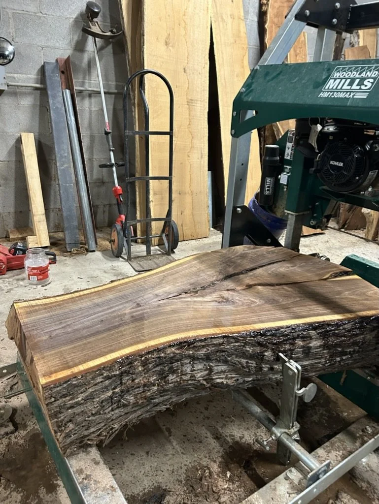 A large, polished slab of wood with natural edges, resting on a woodworking stand in a workshop.