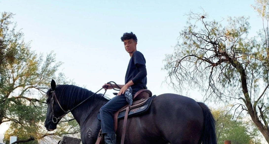 A young man sitting on a black horse outdoors with trees in the background. Darne, Ride Like Darne Scholarship