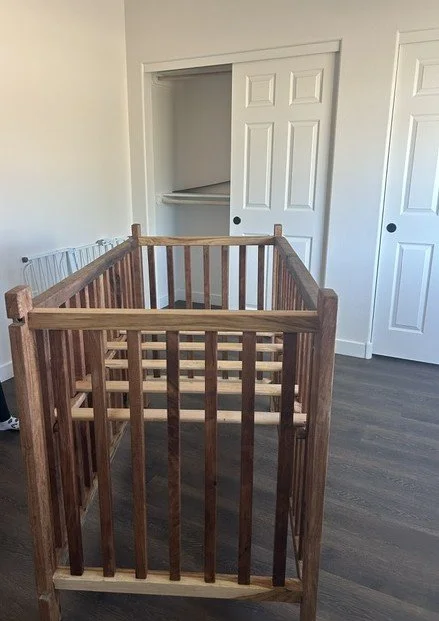Wooden crib frame in a room with white walls and closet doors.