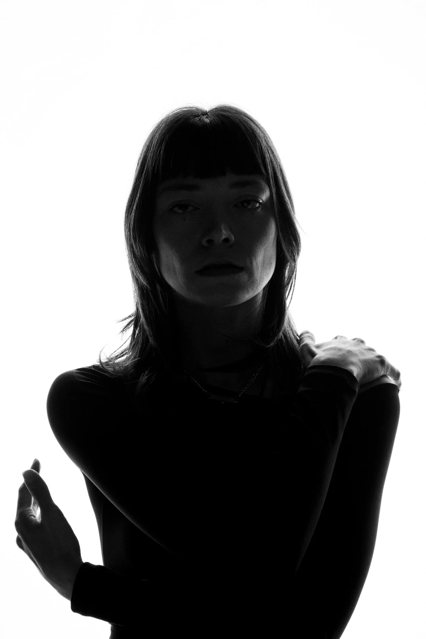 Black and white silhouette of a woman. She has shoulder-length hair with bangs and appears to be holding her hand up with an index finger pointing outward, next to her shoulder.