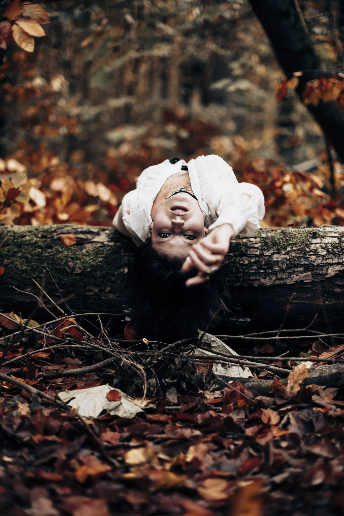 A person lying on a fallen tree trunk in a forest with fallen leaves.