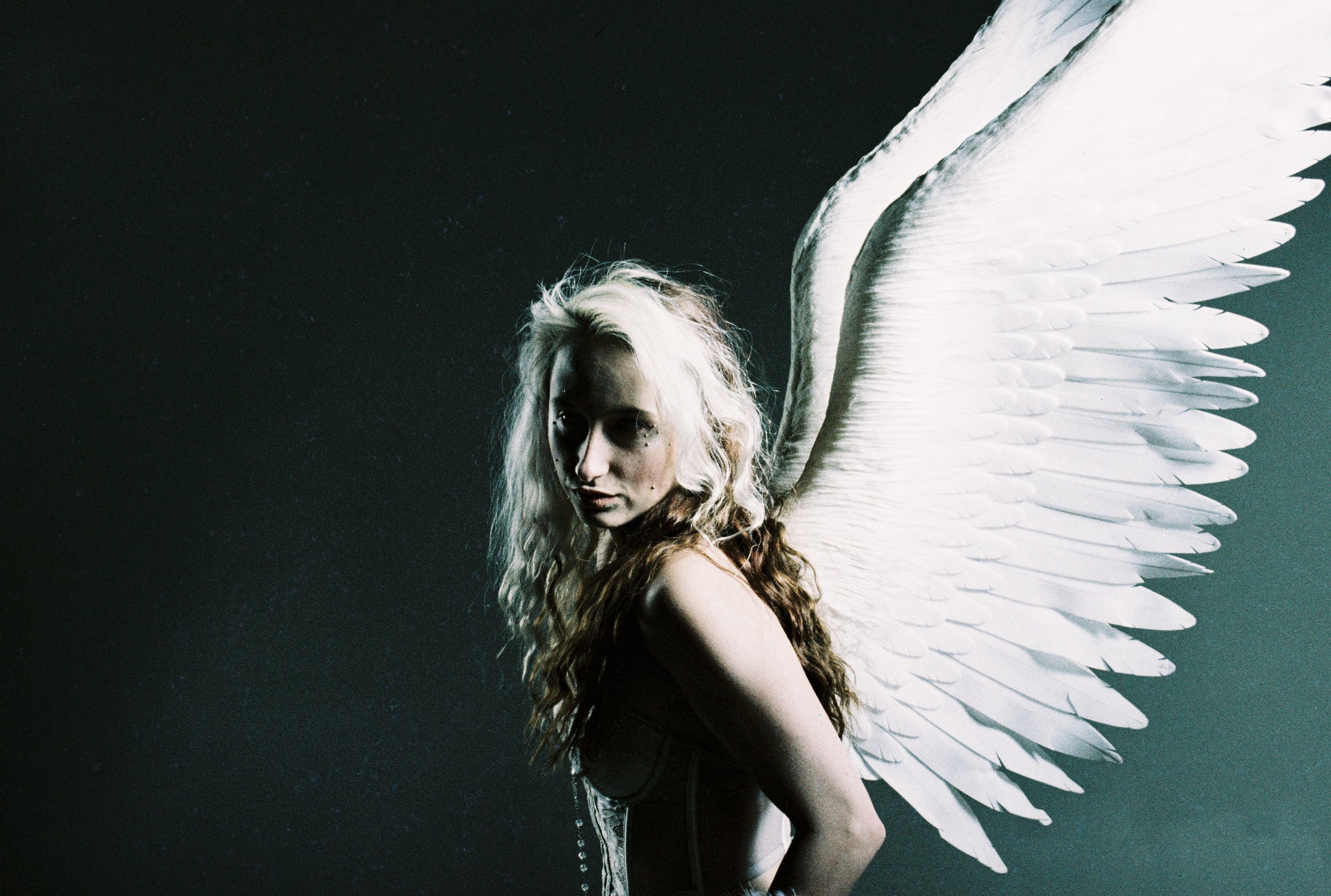 A woman with angel wings posing against a dark background.