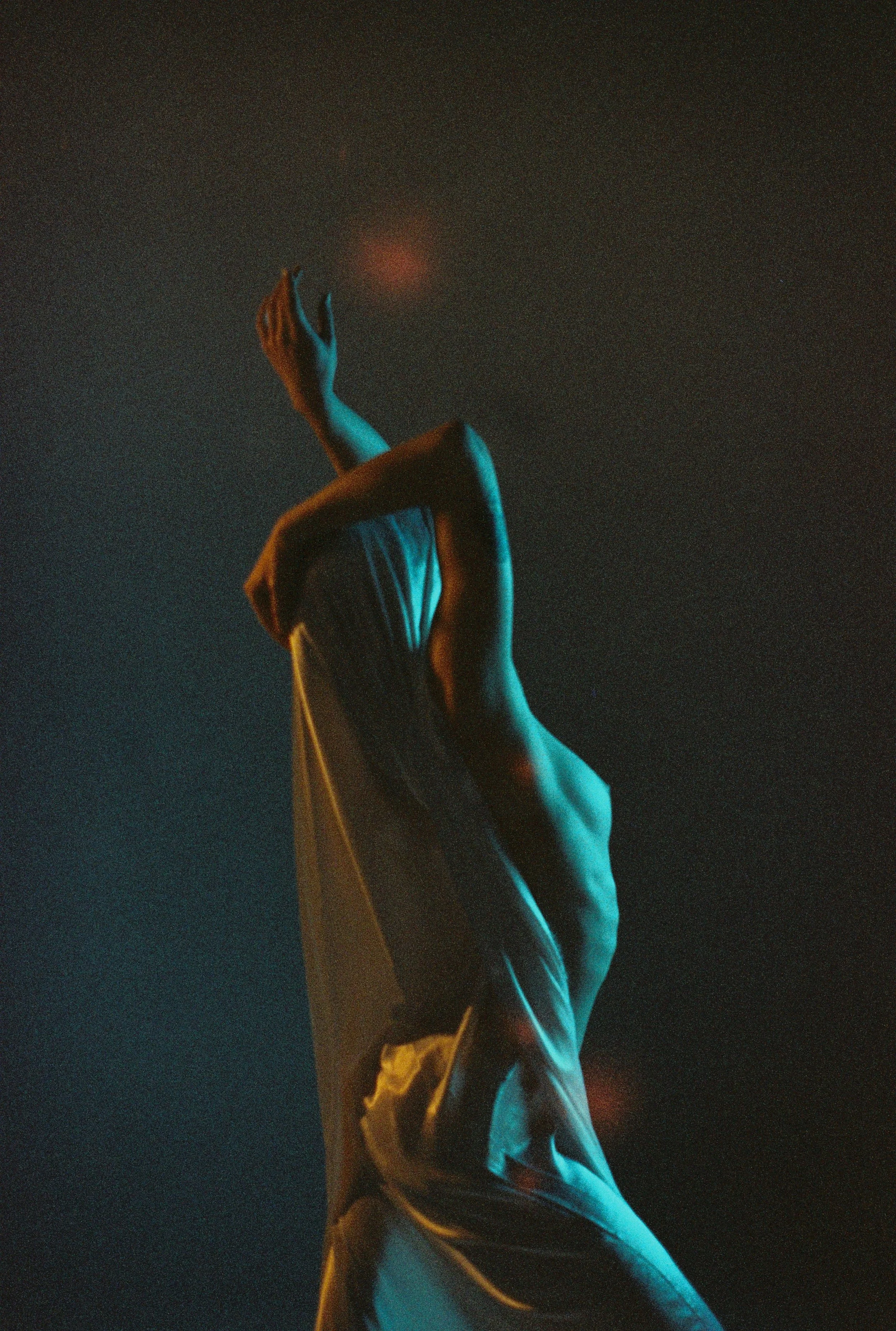 A person dressed in traditional Middle Eastern attire, raising their right hand upwards, with a glowing red light above their palm against a dark background.