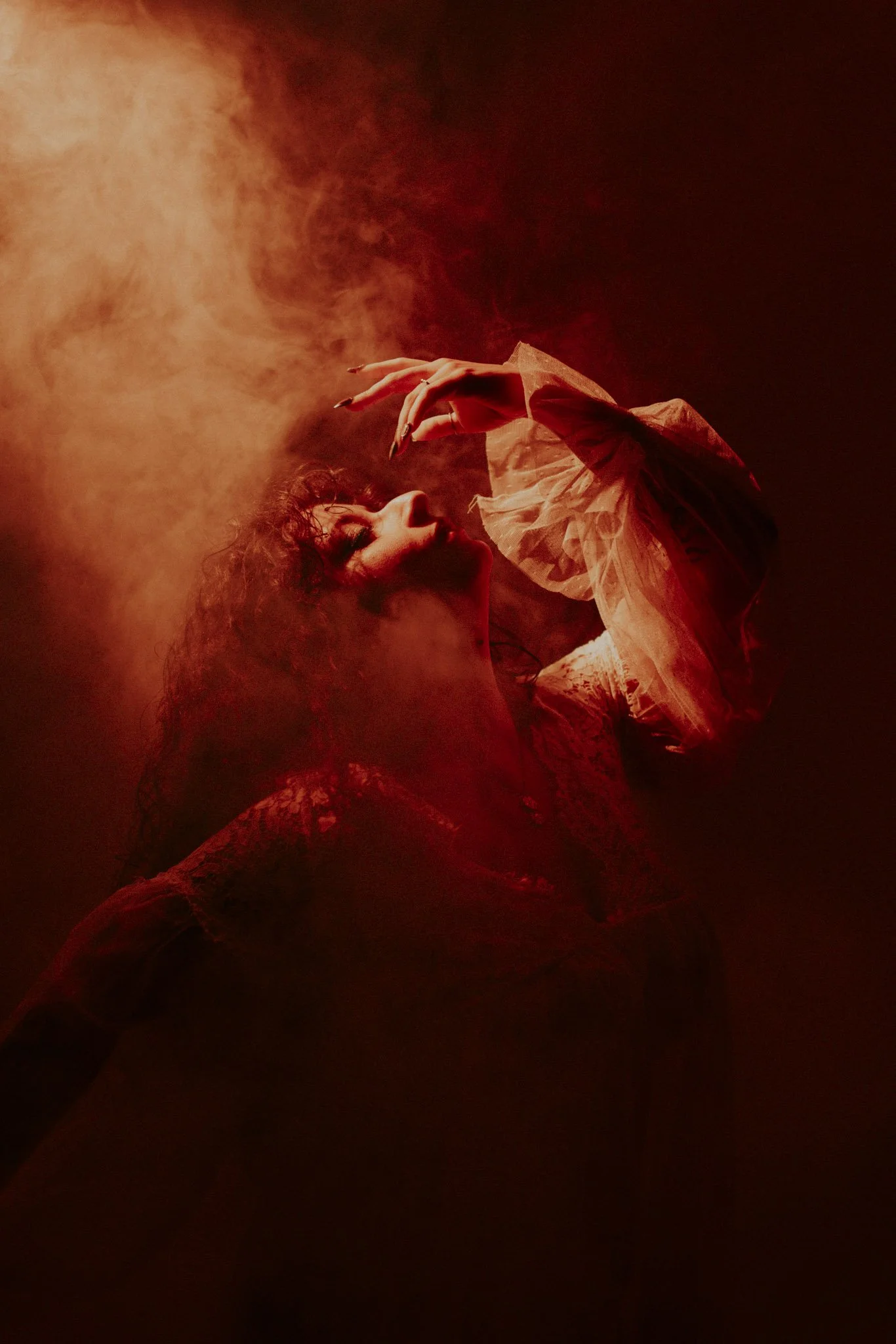 A woman with curly hair and makeup wearing a ruffled sheer dress is performing on stage with red lighting.