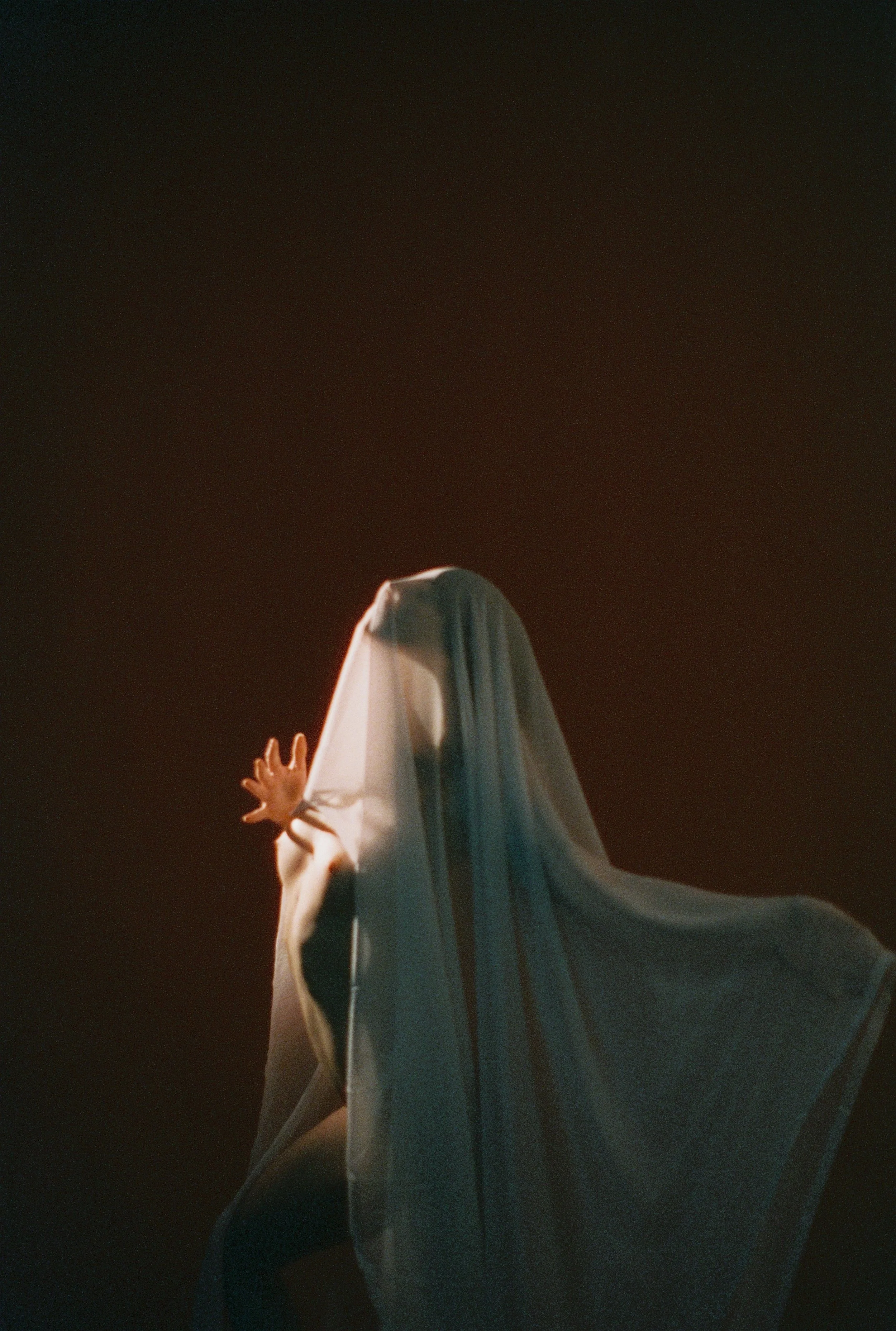 A person dressed as a ghost with a white sheet during a night event, with their hand raised and dark sky background.
