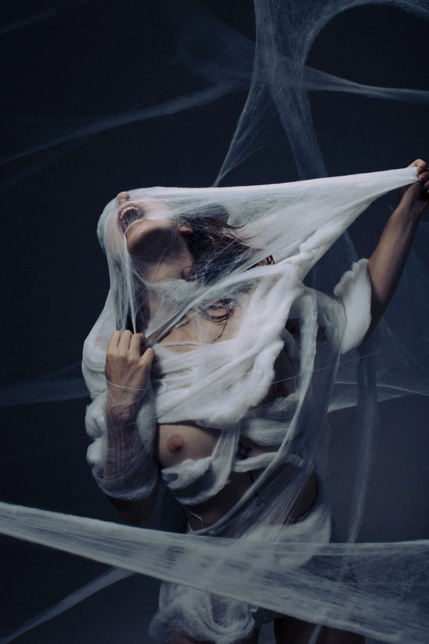 A person with long hair and no shirt is caught behind a transparent plastic sheet, with their mouth open and head tilted back.