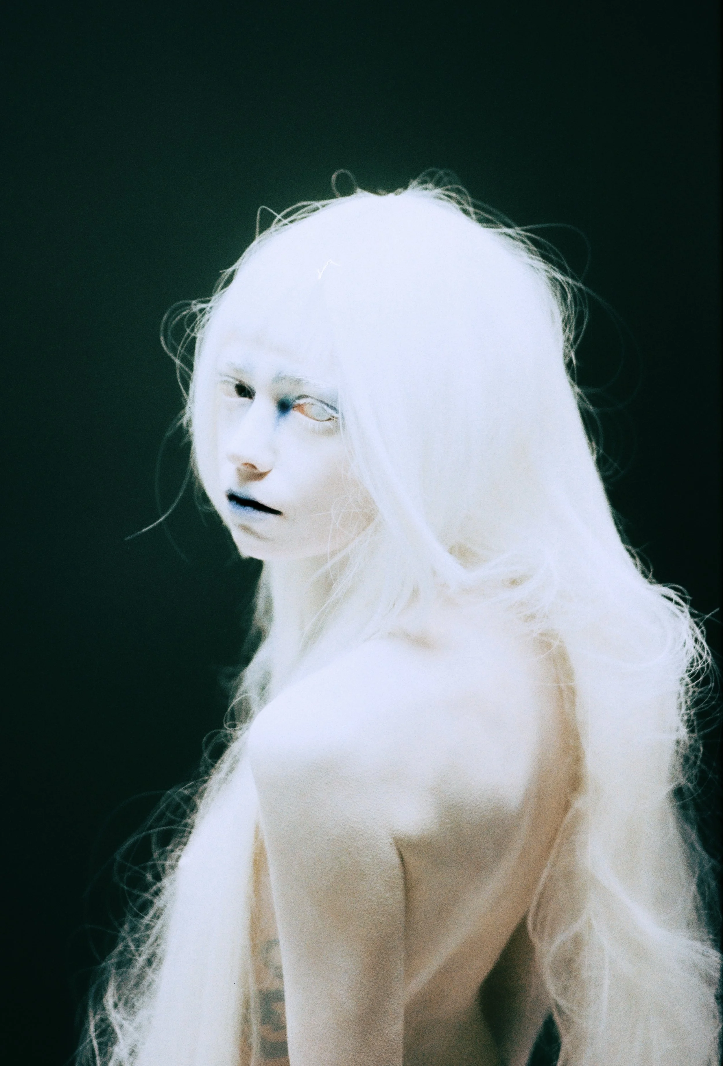 A stylized digital portrait of a woman with long, wavy light-colored hair and a pale complexion, gazing over her shoulder against a dark background.