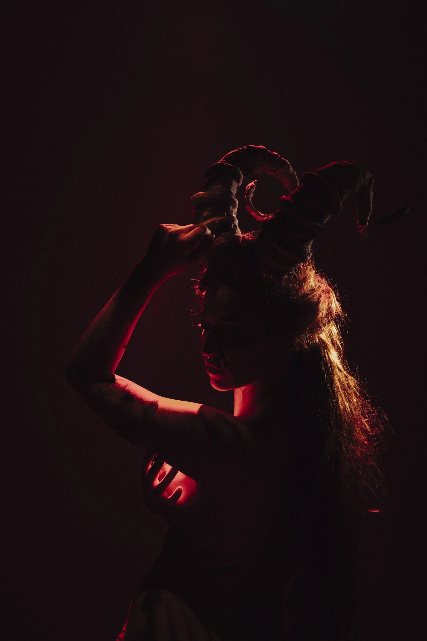 A person with long hair is holding a cupcake with a candle on top, silhouetted against a dark background with red lighting.