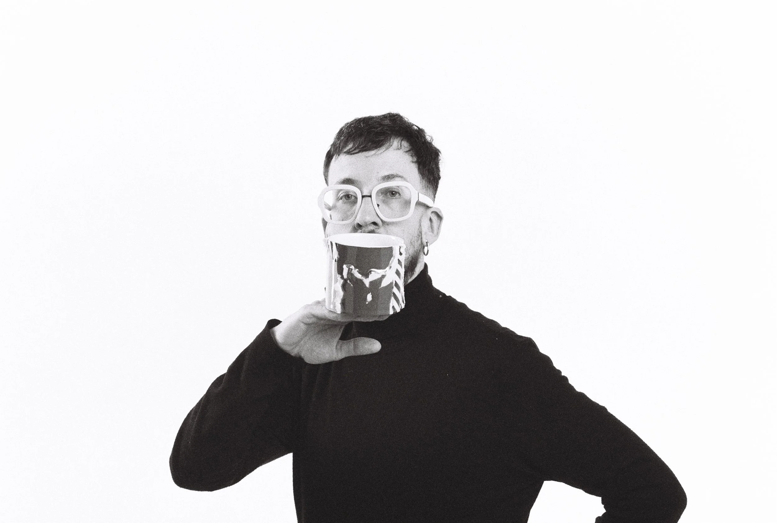 A person with short dark hair wearing glasses and a black top, holding a large mug with a lion face design, against a plain white background.