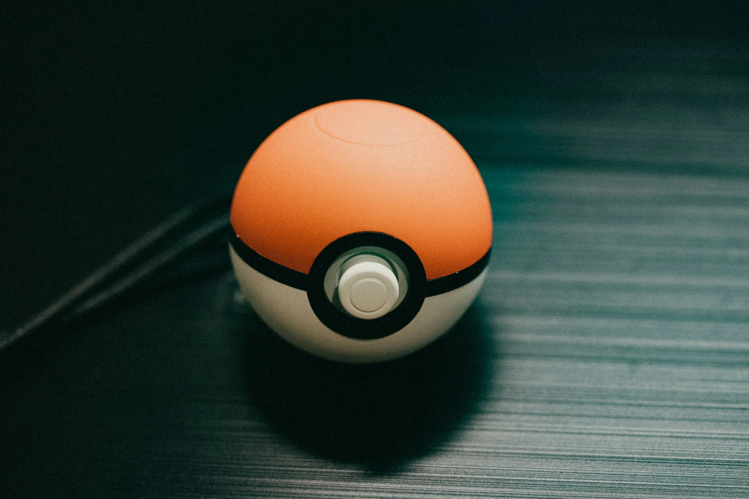 A close-up of a Poké Ball from the Pokémon series, resting on a dark, textured surface.