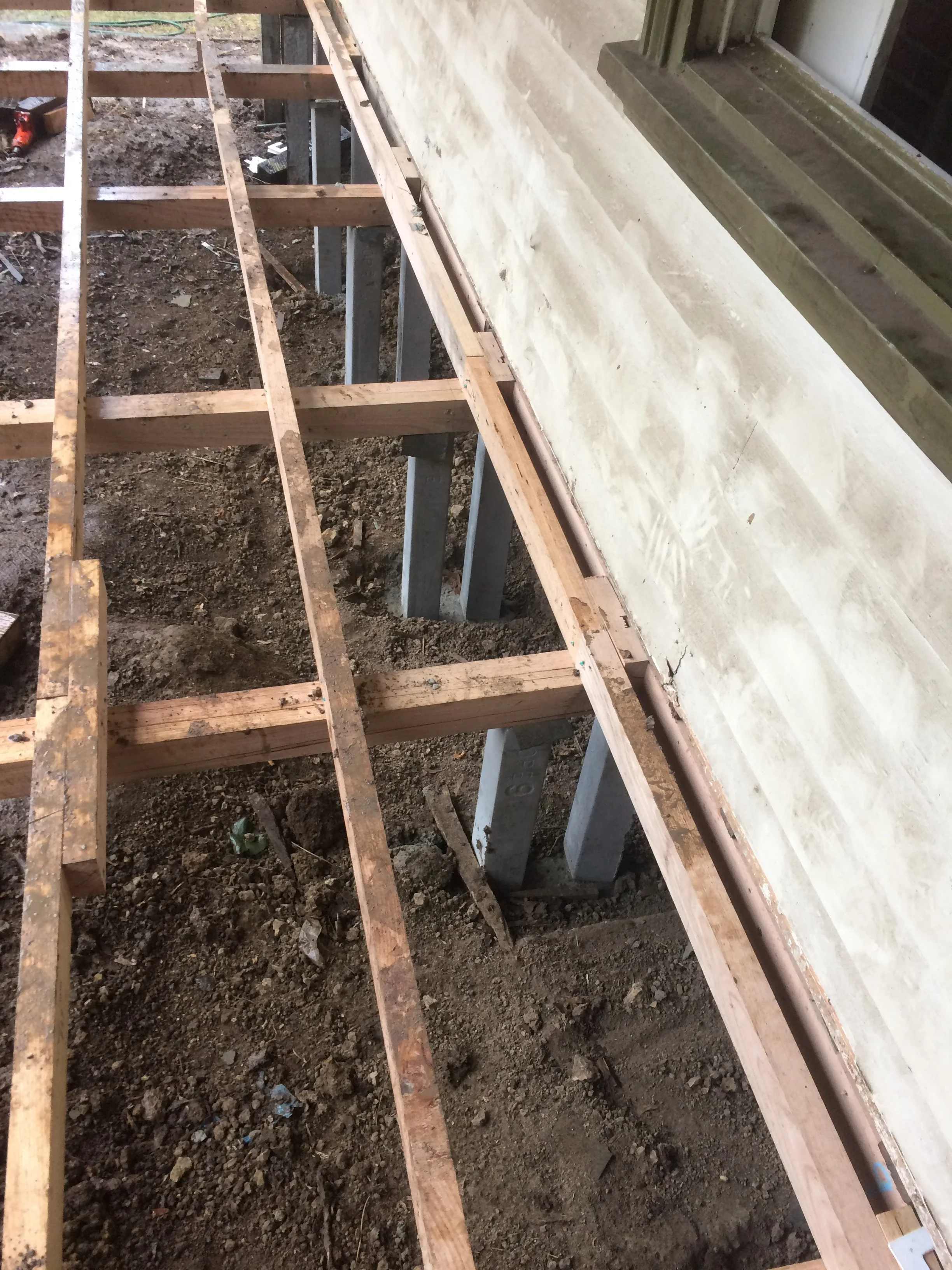 Construction site with wooden framework, dirt ground, and a concrete wall with a copper pipe along the base.