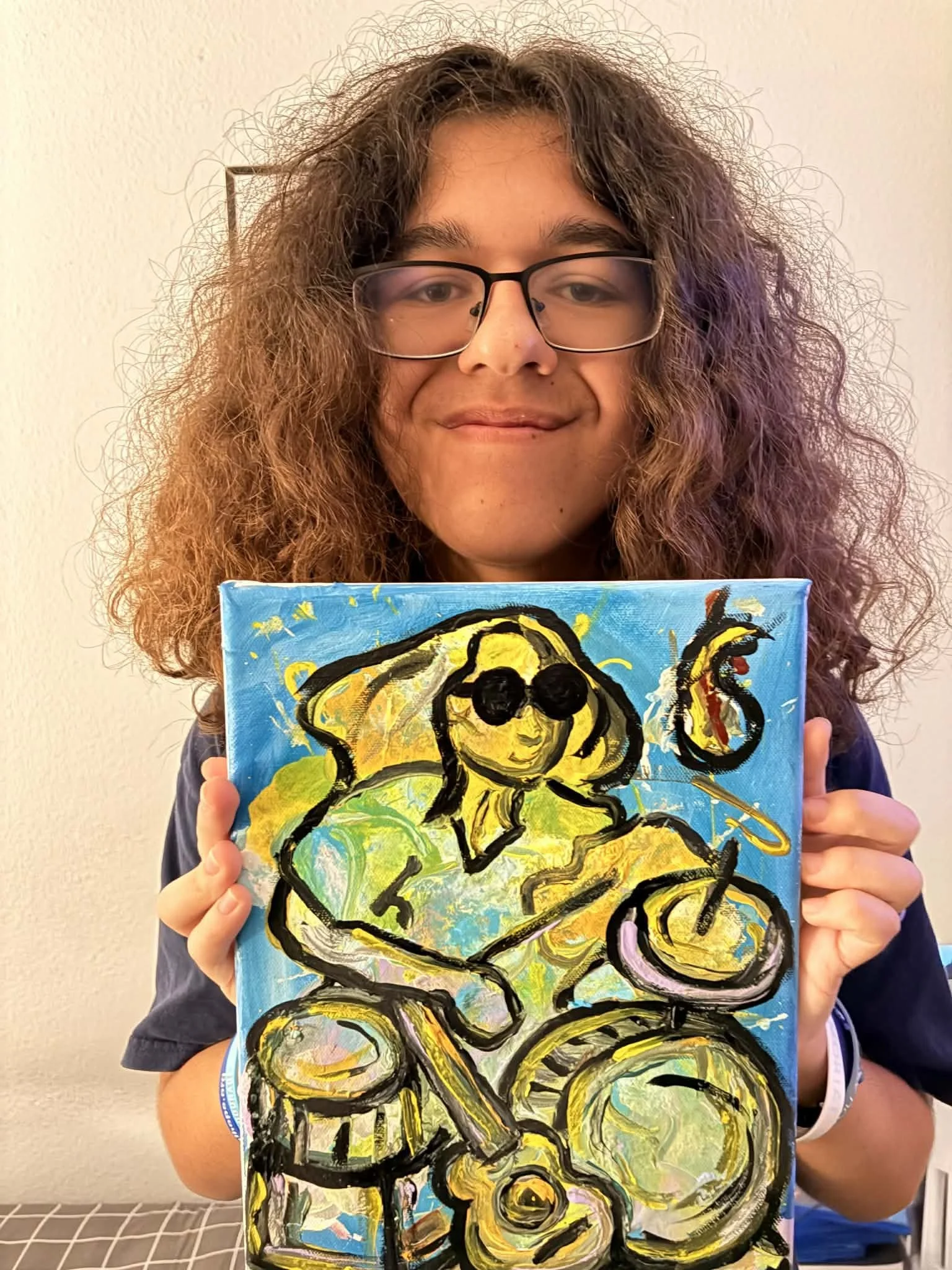 Person wearing glasses holding a colorful abstract painting of a smiling figure with curly hair, against a plain wall background.