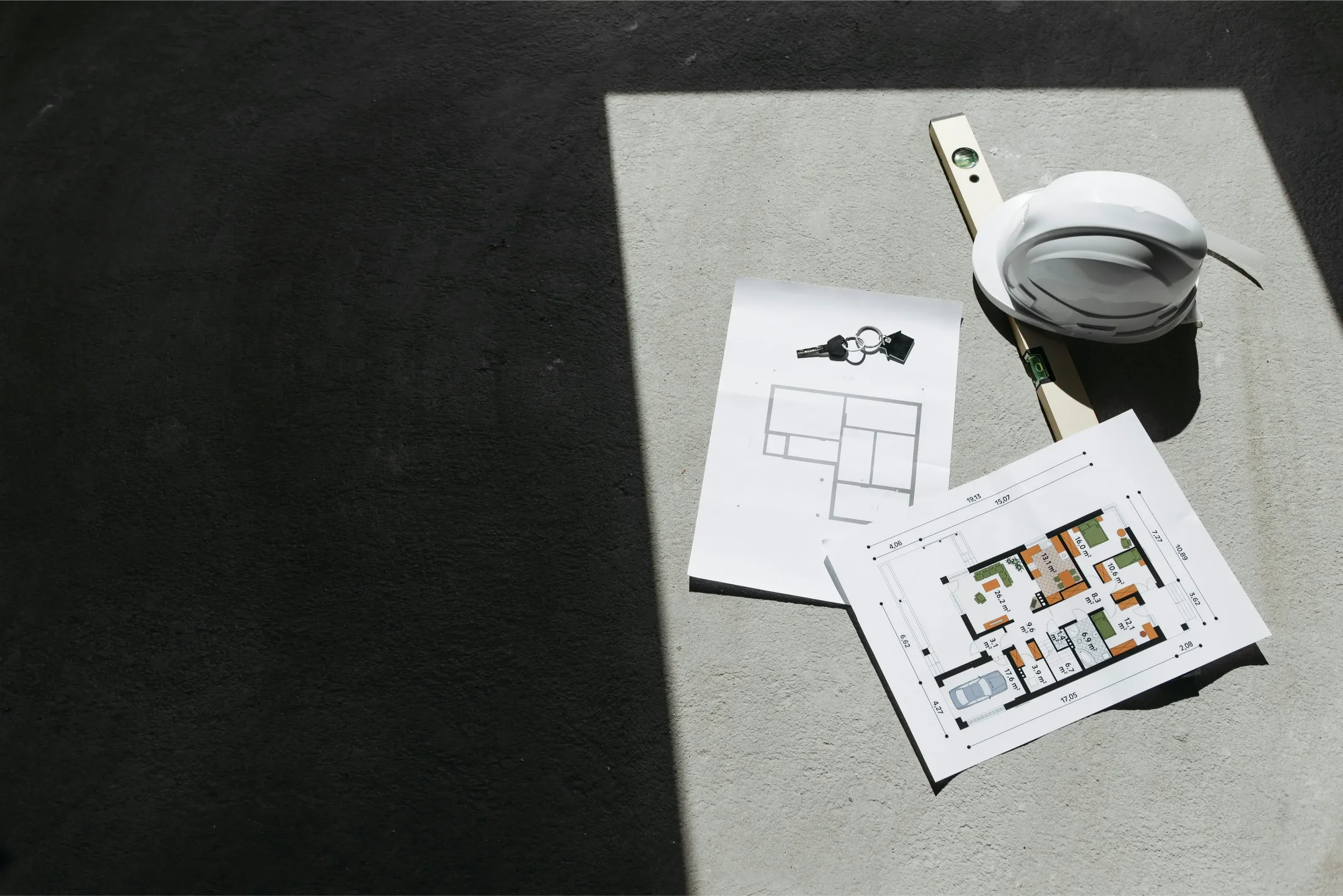 Architectural floor plans and a set of keys on a concrete surface with a mixing of sunlight and shadow.