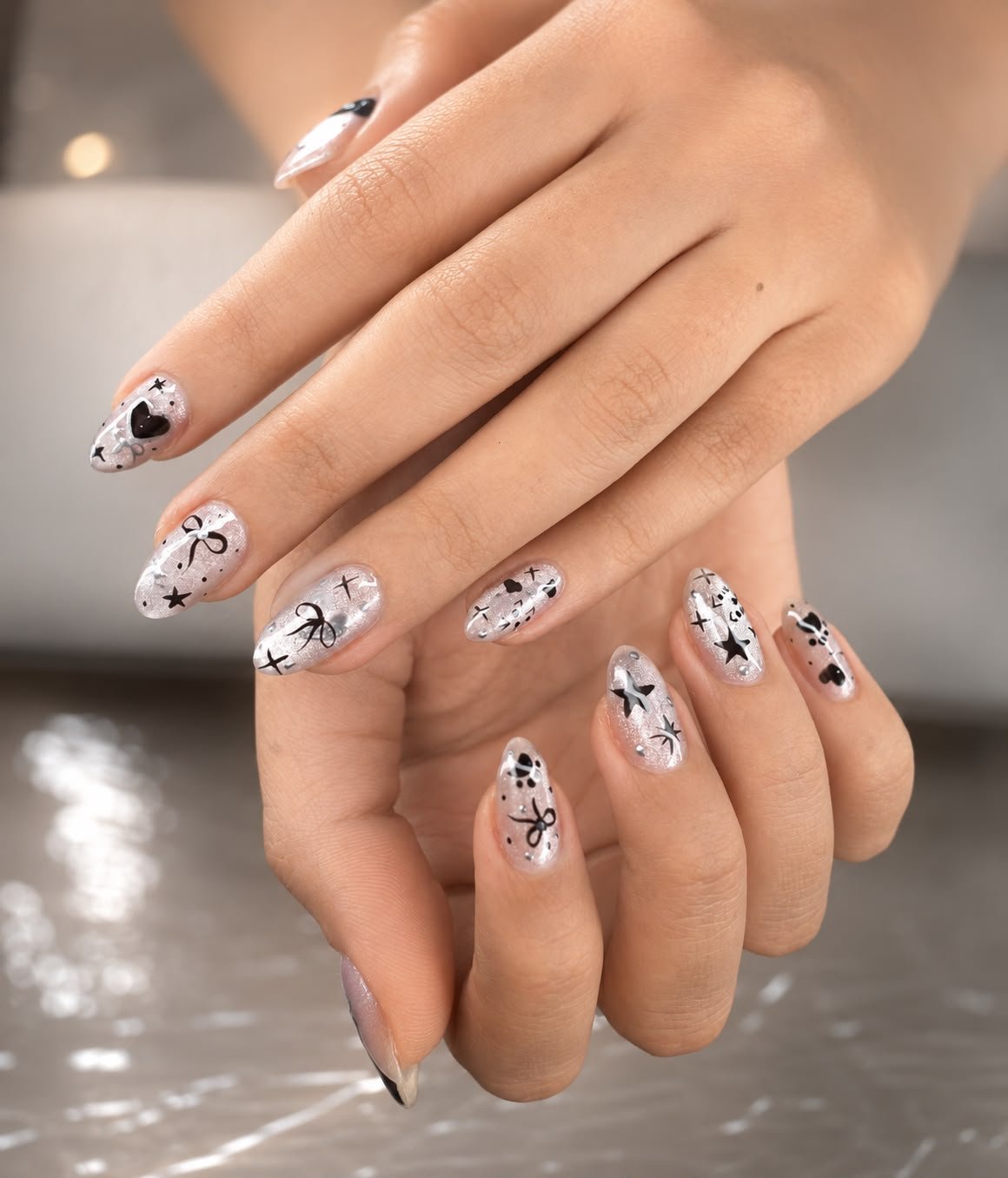 Close-up of hands with decorated nails featuring black and white designs, including bows, stars, and hearts on a shiny, clear base.