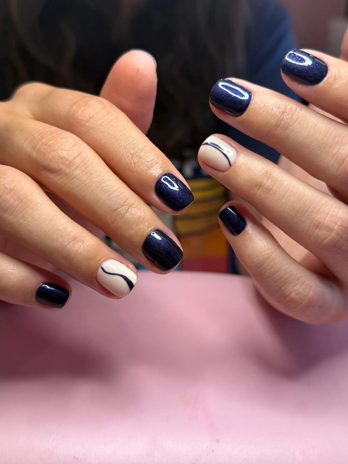 Close-up of hands with manicured nails, featuring navy blue polish with white accents and blue line designs.