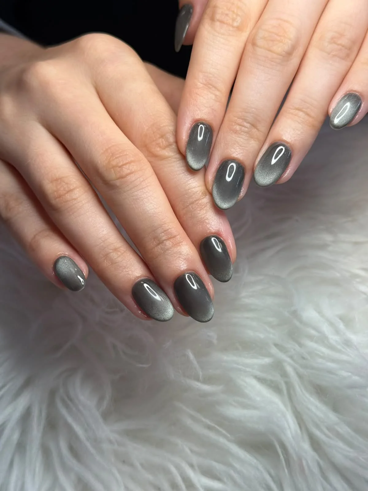 Close-up of hands with nails painted in a black to silver gradient, resting on a white fluffy surface.