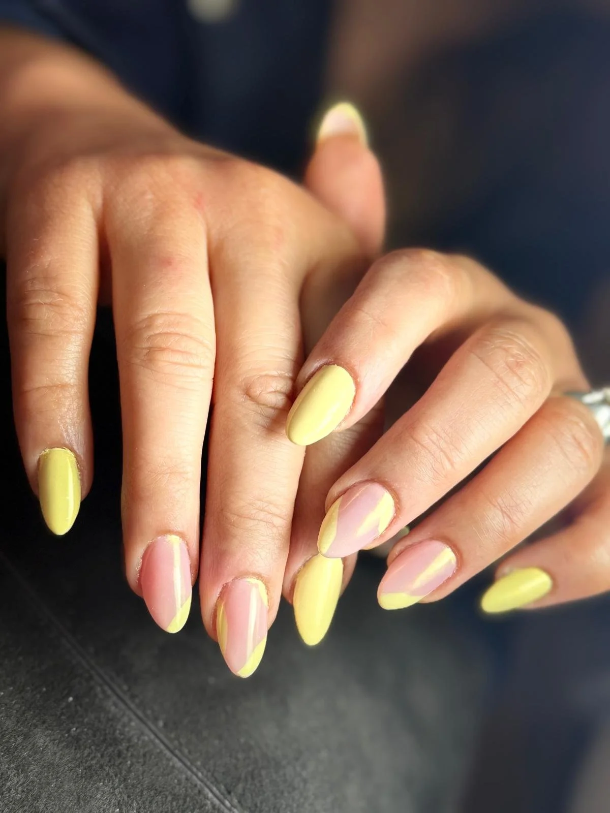 Close-up of a person's hand with yellow and pink nail polish, resting on a dark surface.