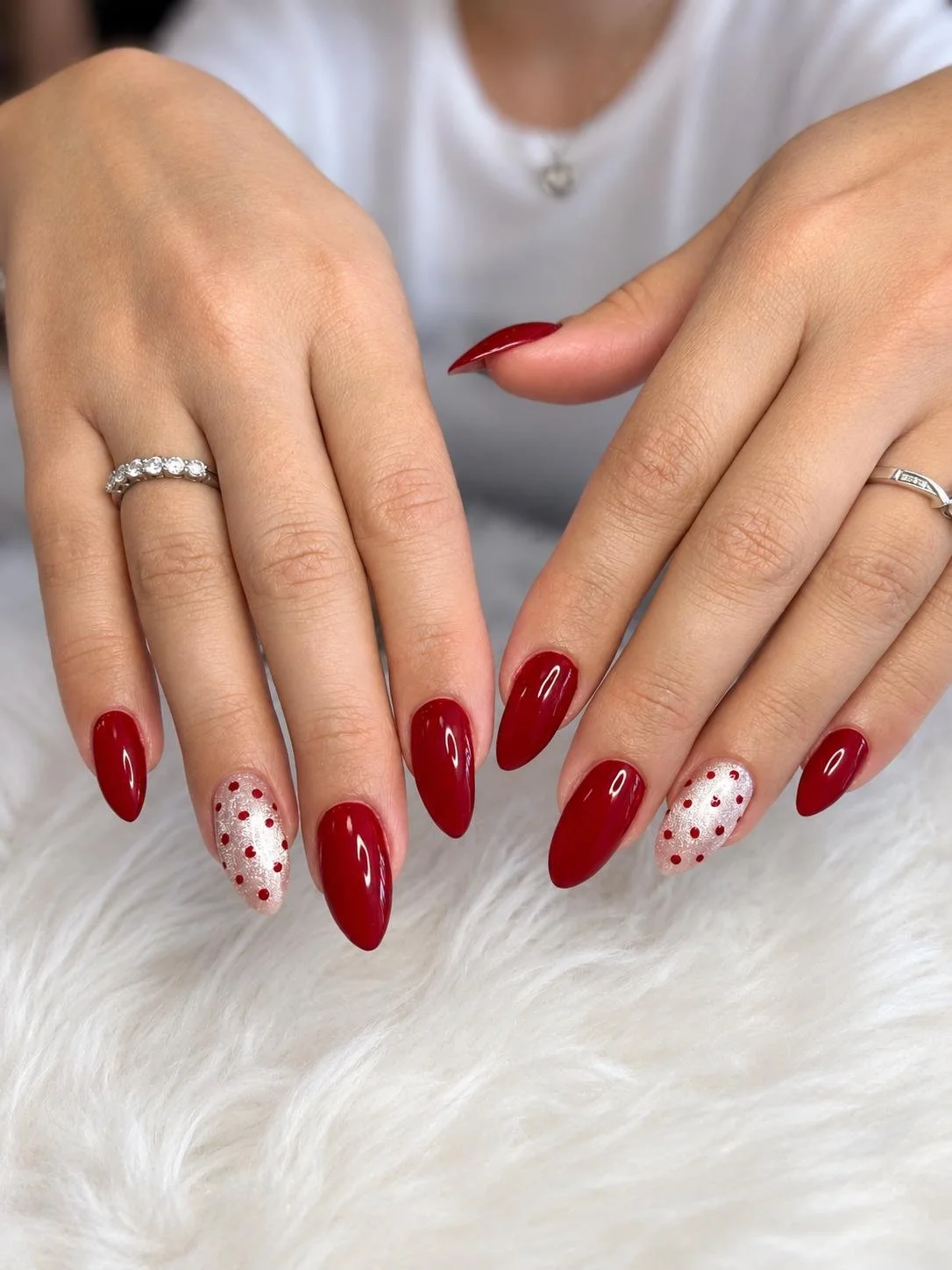 Close-up of a woman's hands showing red and white polka dot manicure, silver rings, and a white shirt.