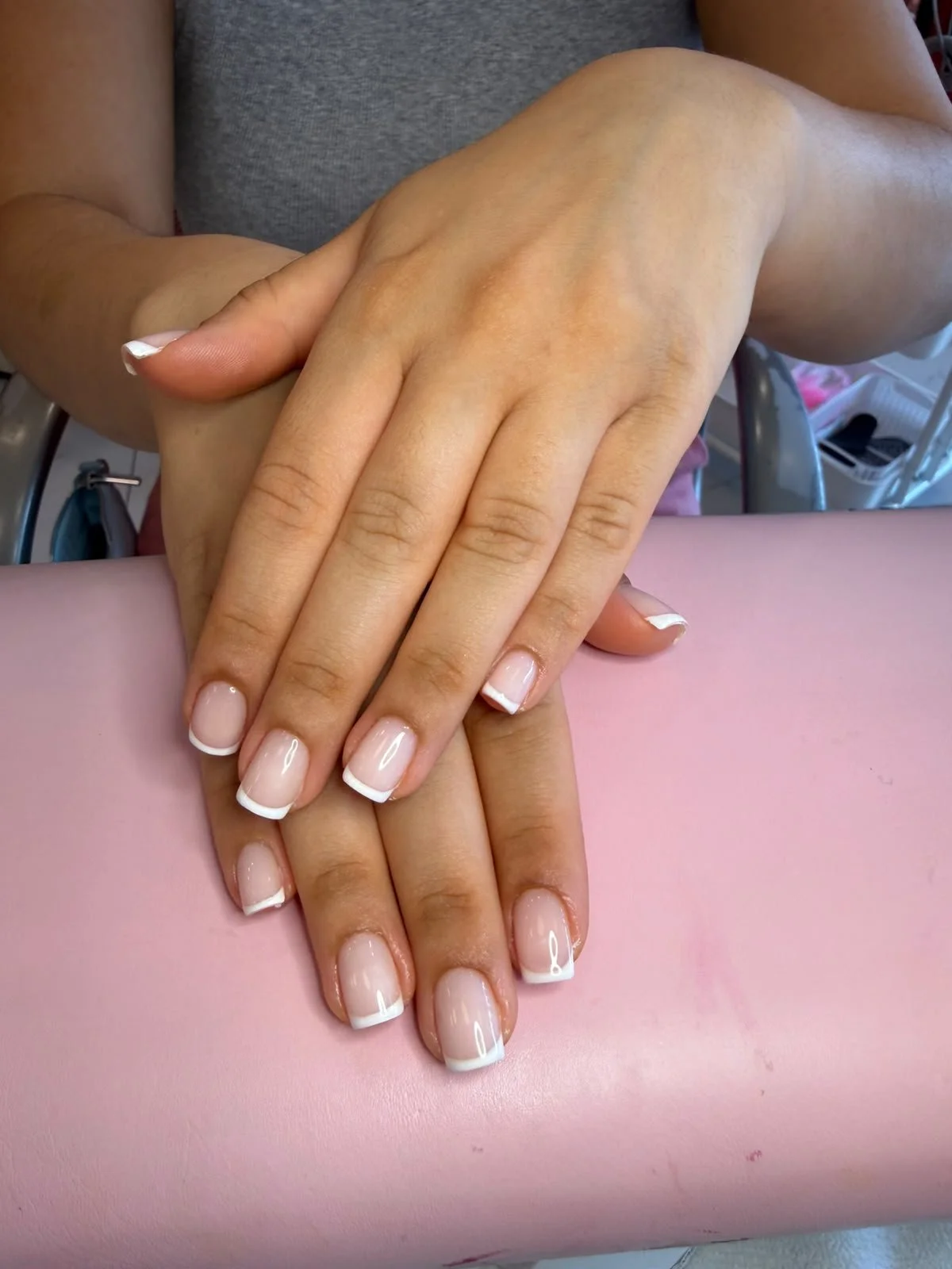 Close-up of a person's hands resting on a pink surface, showing freshly manicured nails with French tips.