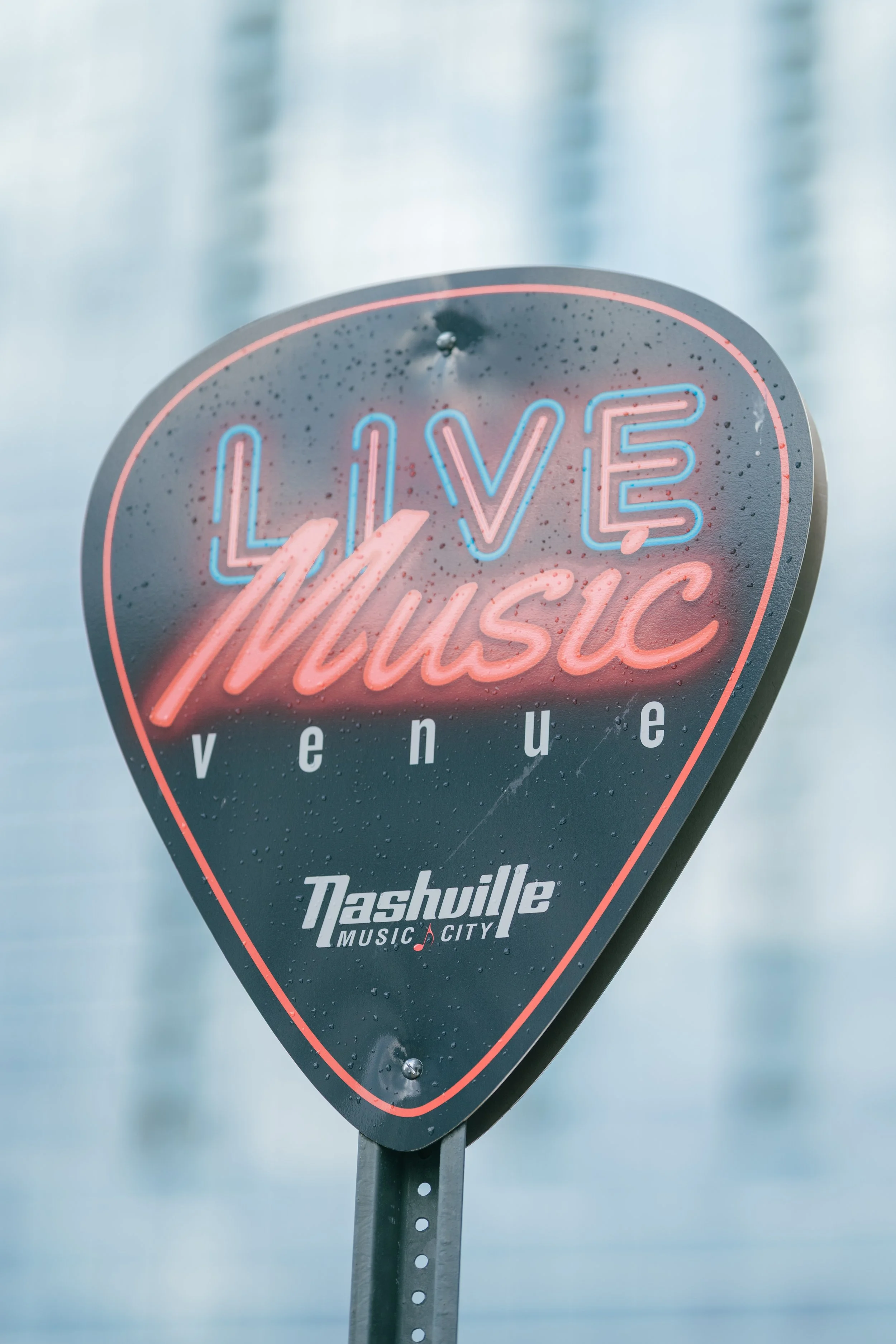 Neon sign reading 'Love Music' with 'Nashville Music City' logo, mounted on a street pole, with rain droplets on the sign
