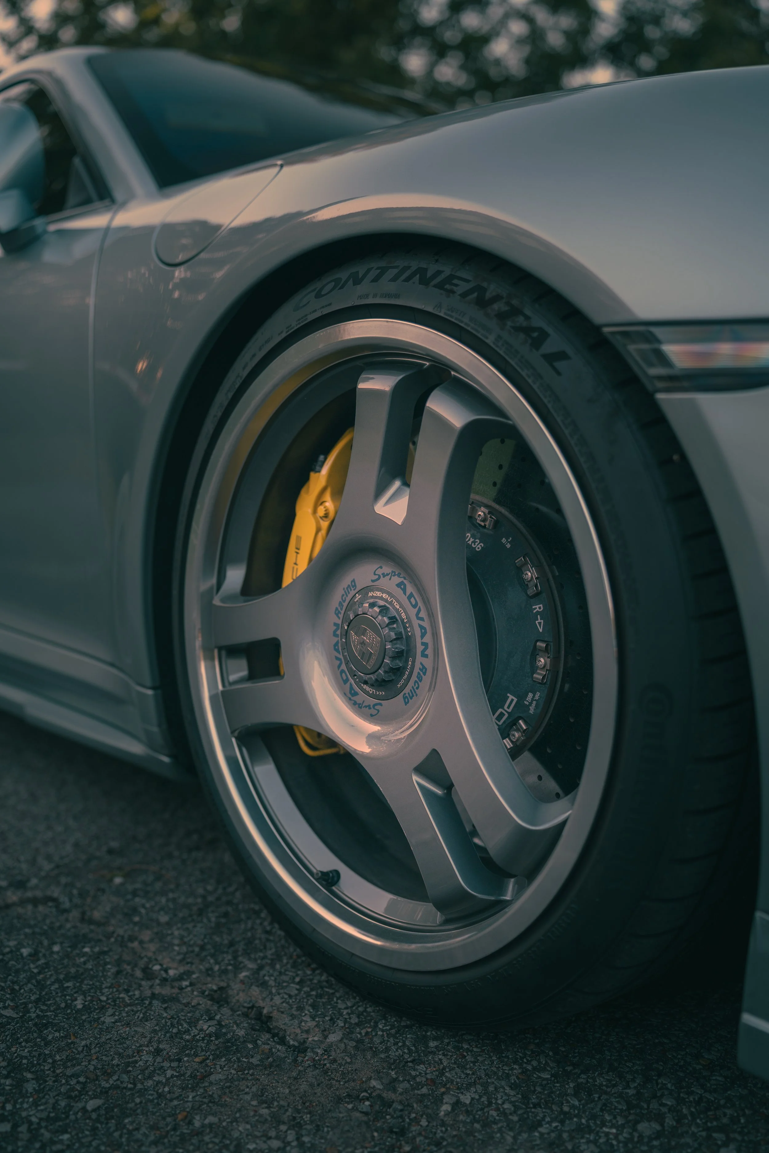 Close-up of a luxury sports car wheel with a large silver rim, yellow brake caliper, and Continental tire, parked on asphalt.