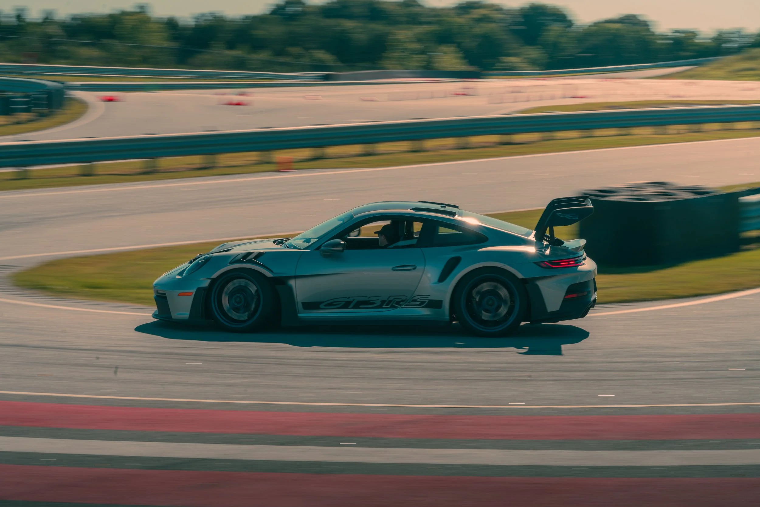 Gray sports car racing on a track with blurred background, indicating high speed, during daytime.