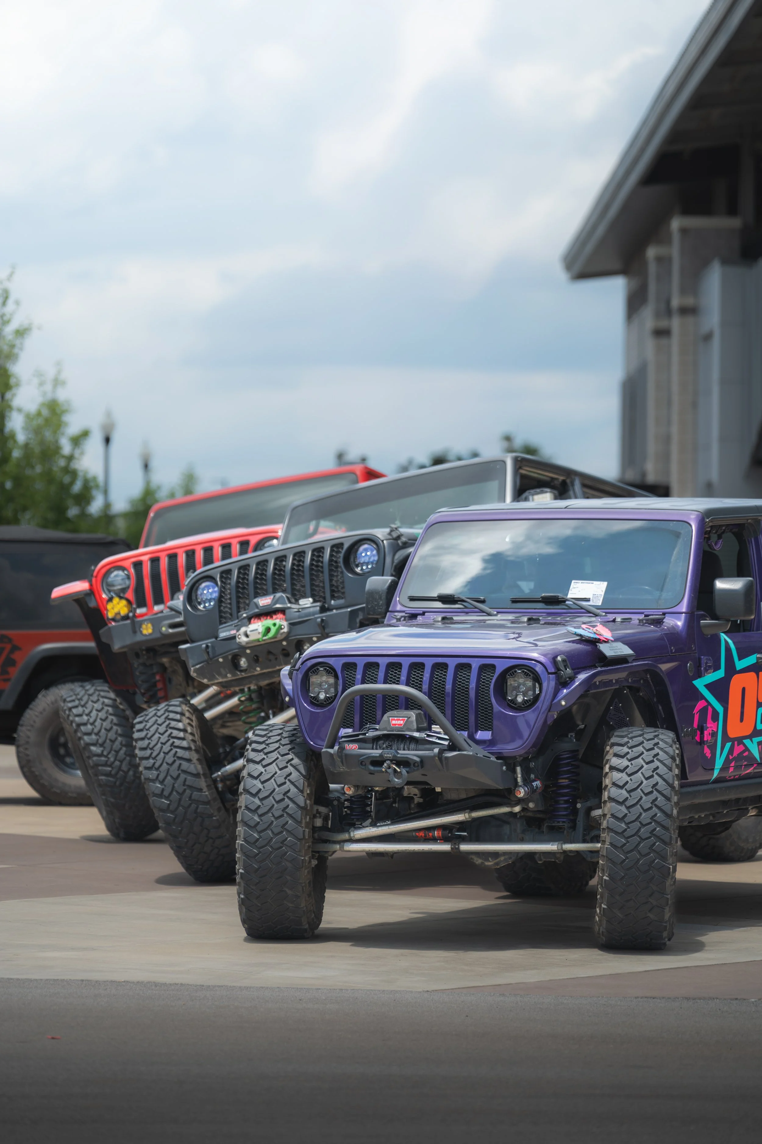 A row of colorful off-road vehicles parked outdoors, with a cloudy sky and a building in the background.