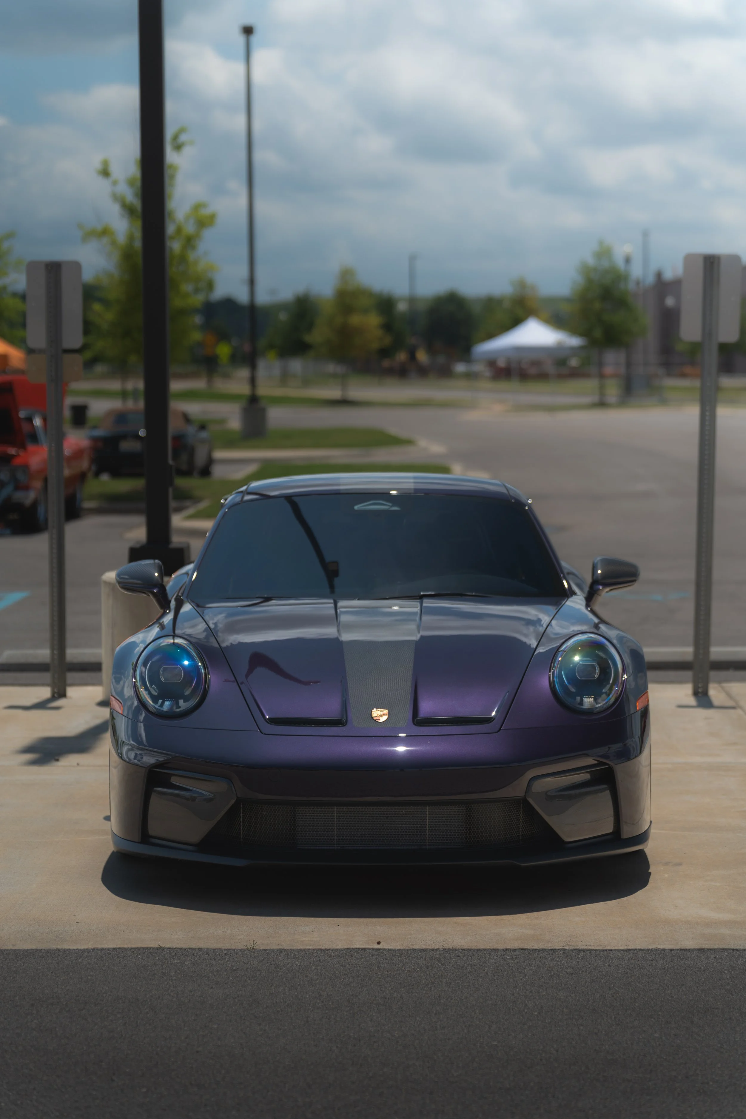 A black Porsche sports car parked in a parking lot with a blue sky and some clouds, surrounded by trees and other parked cars.