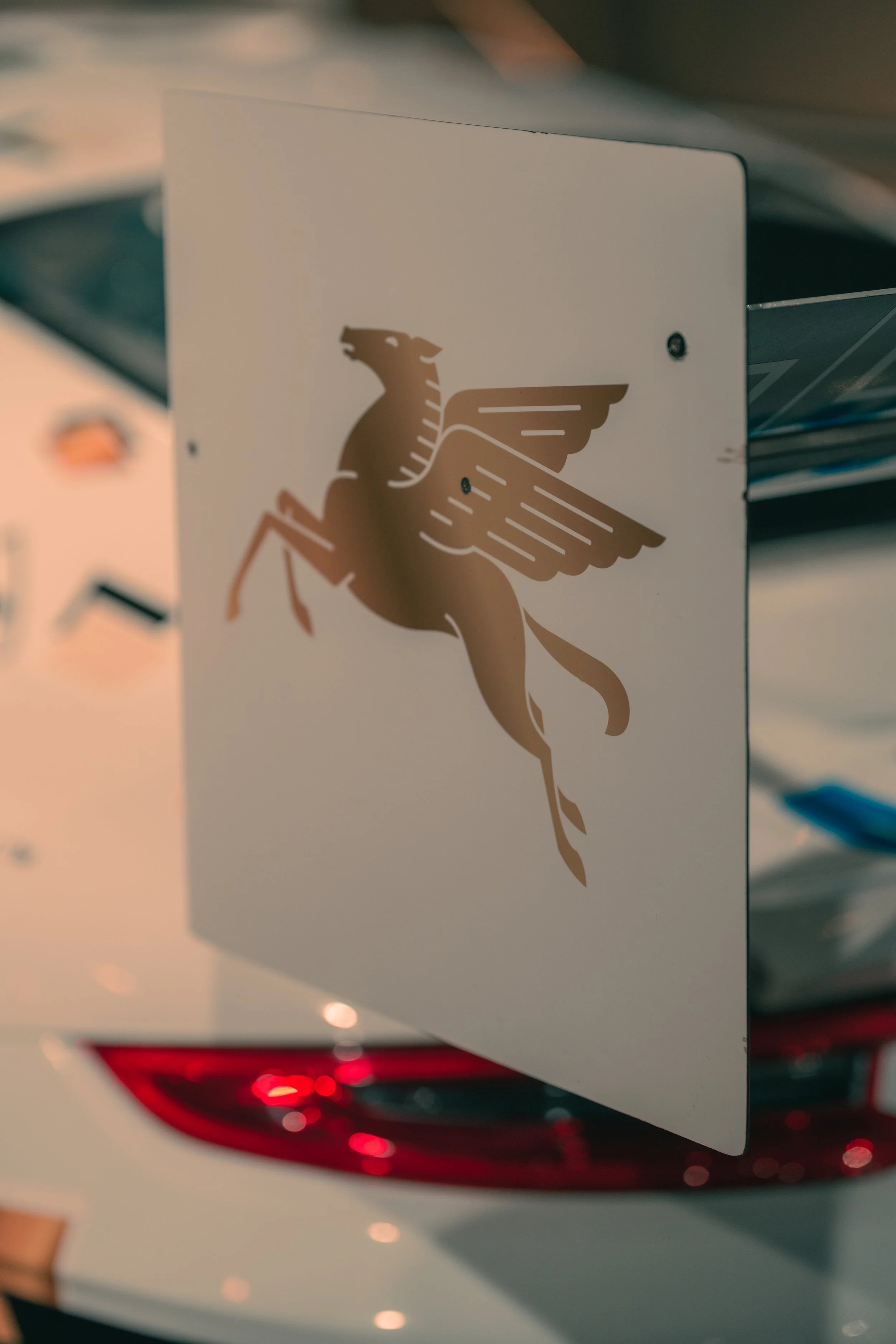 Close-up of a white car with a sticker of a winged lion on the rear window.