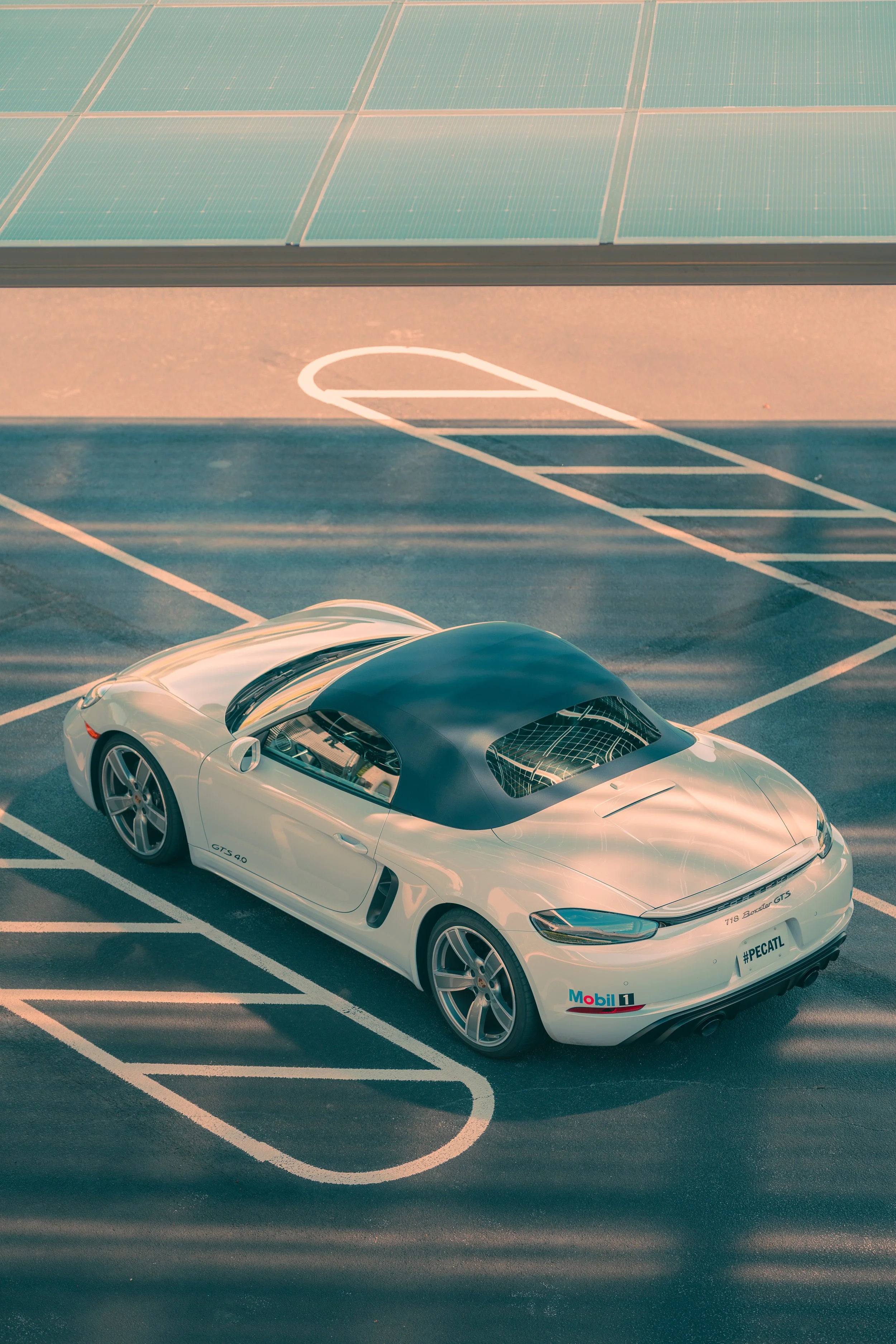 A white sports car with a black roof parked in a nearly empty parking lot under solar panels.