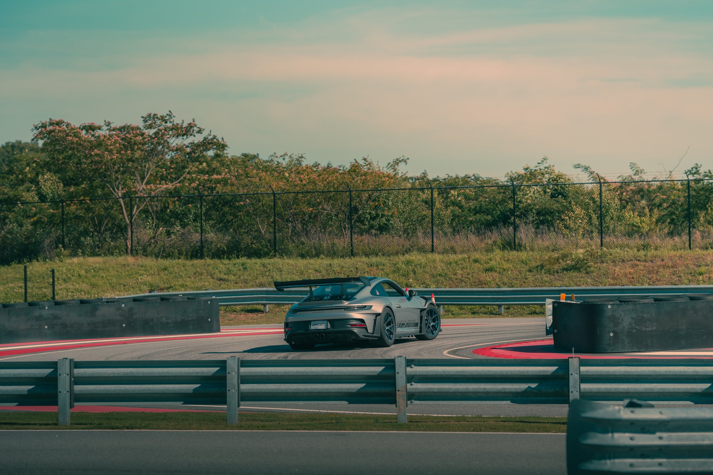A silver sports car on a racetrack, with trees and a sky in the background.