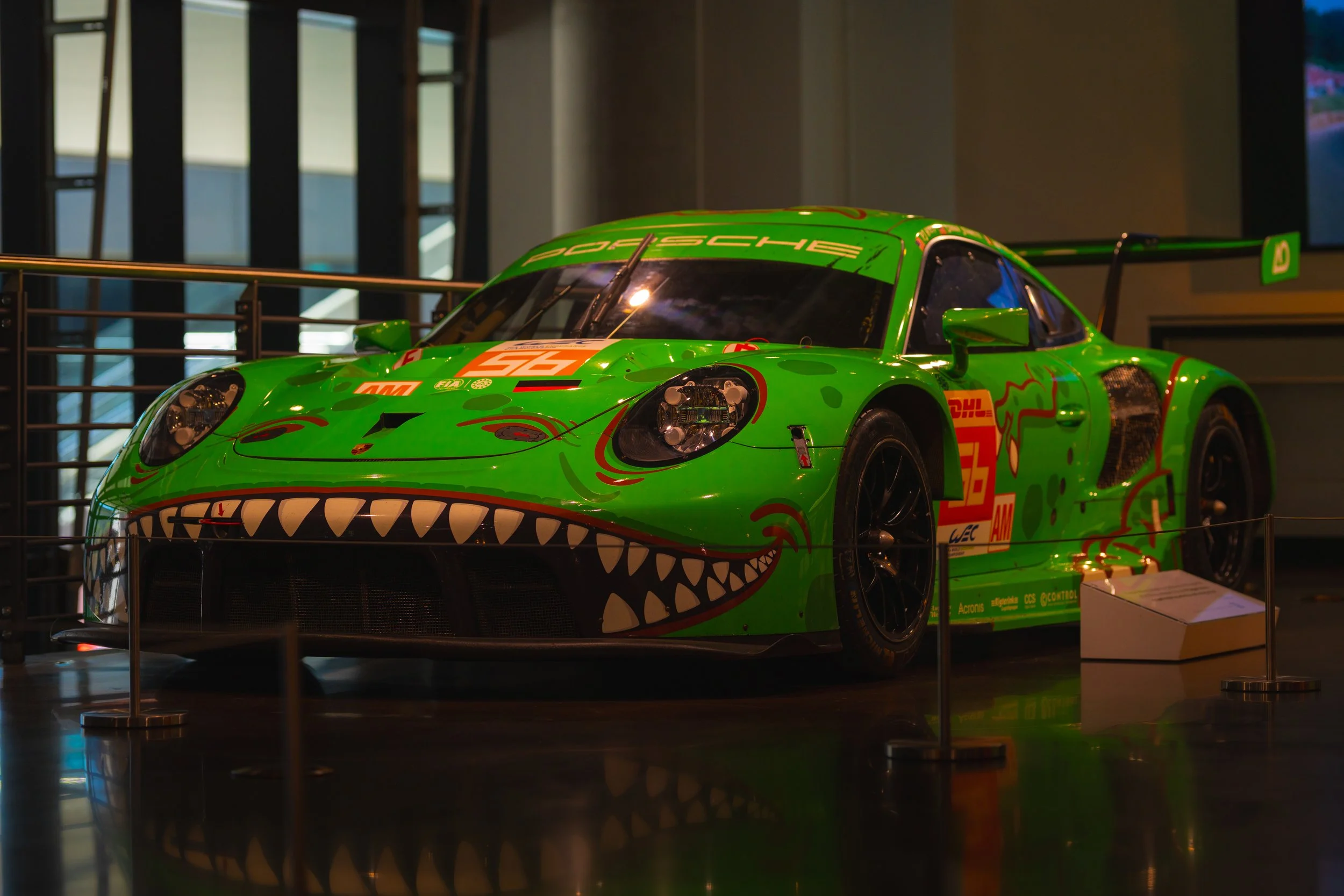 A bright green race car with a dinosaur face painted on the front, displayed indoors behind a metal barrier.