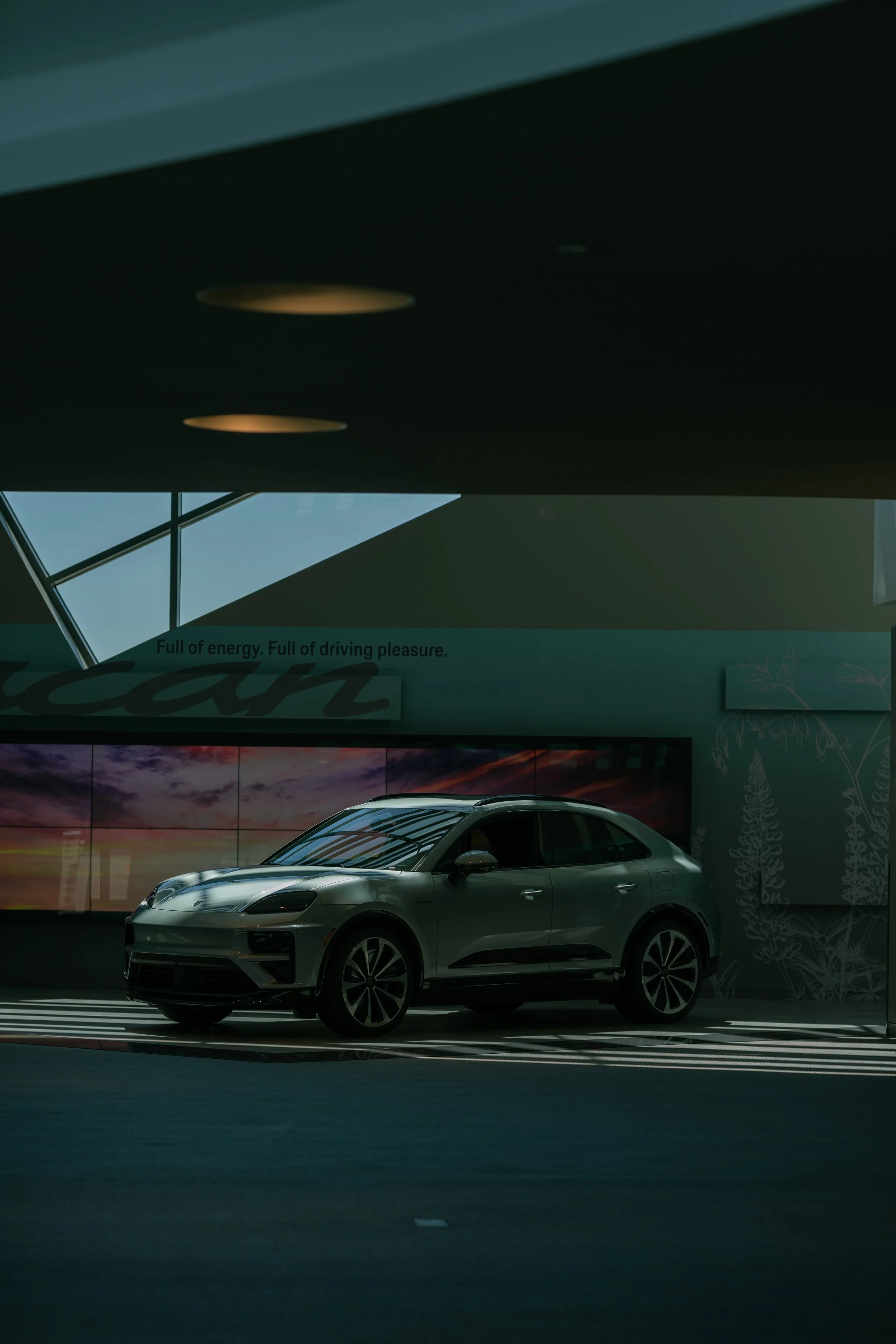 Silver SUV parked indoors with a digital display showing a sunset and a motivational quote about energy and driving pleasure.