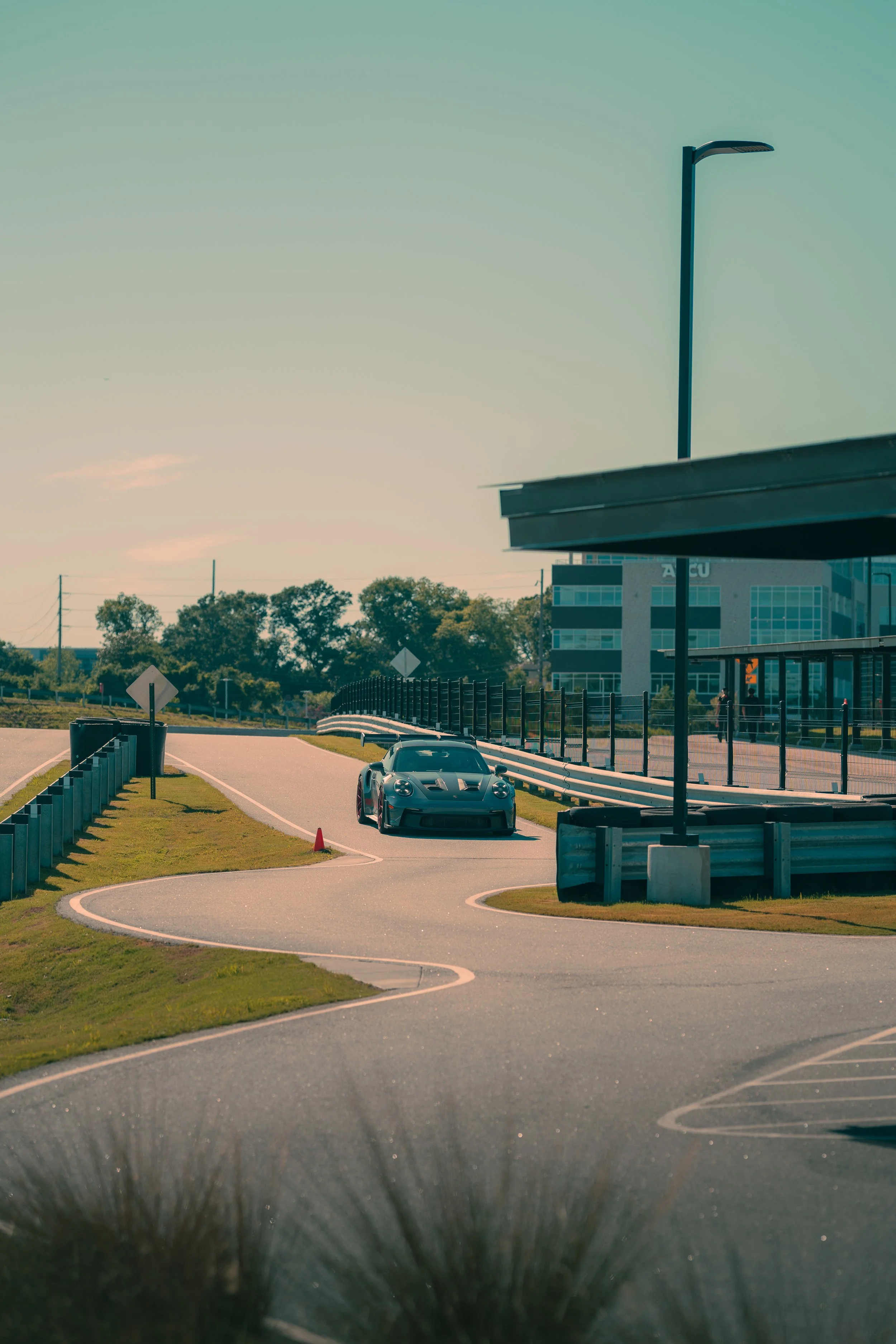 A black sports car parked near a curved road in an urban setting with a modern building in the background and a streetlight above.