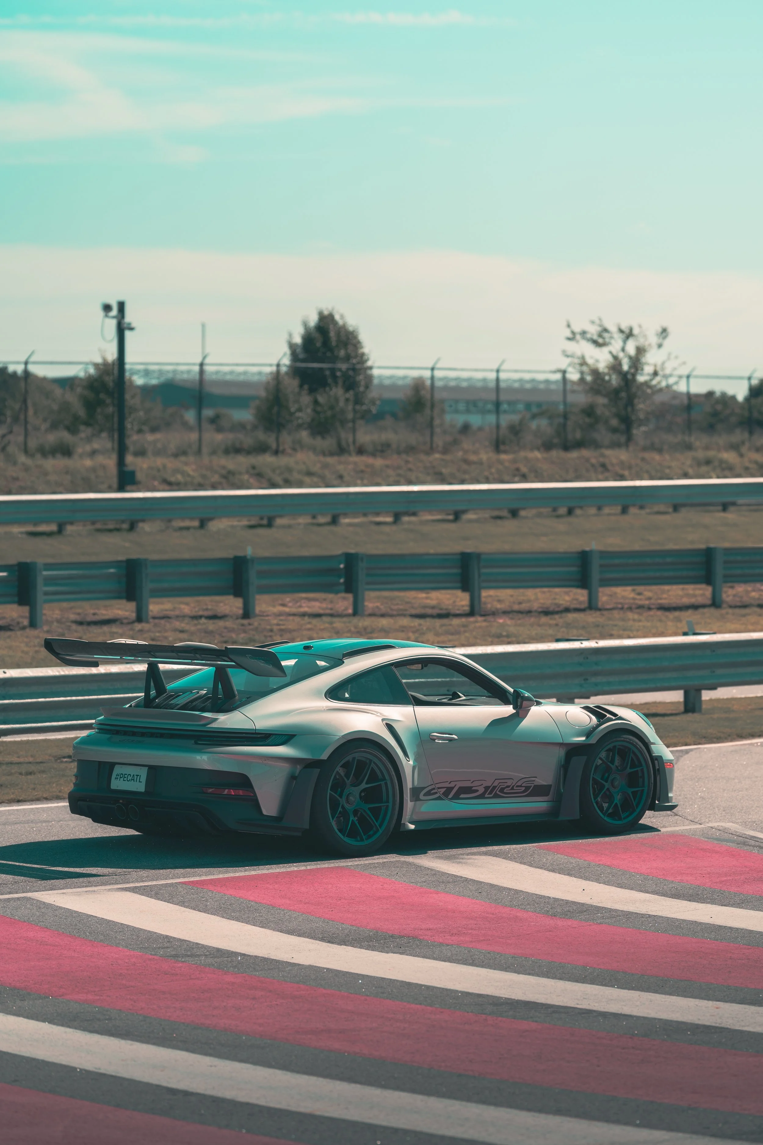 A silver sports car with a large rear wing, parked on a racetrack with painted red and white lines.