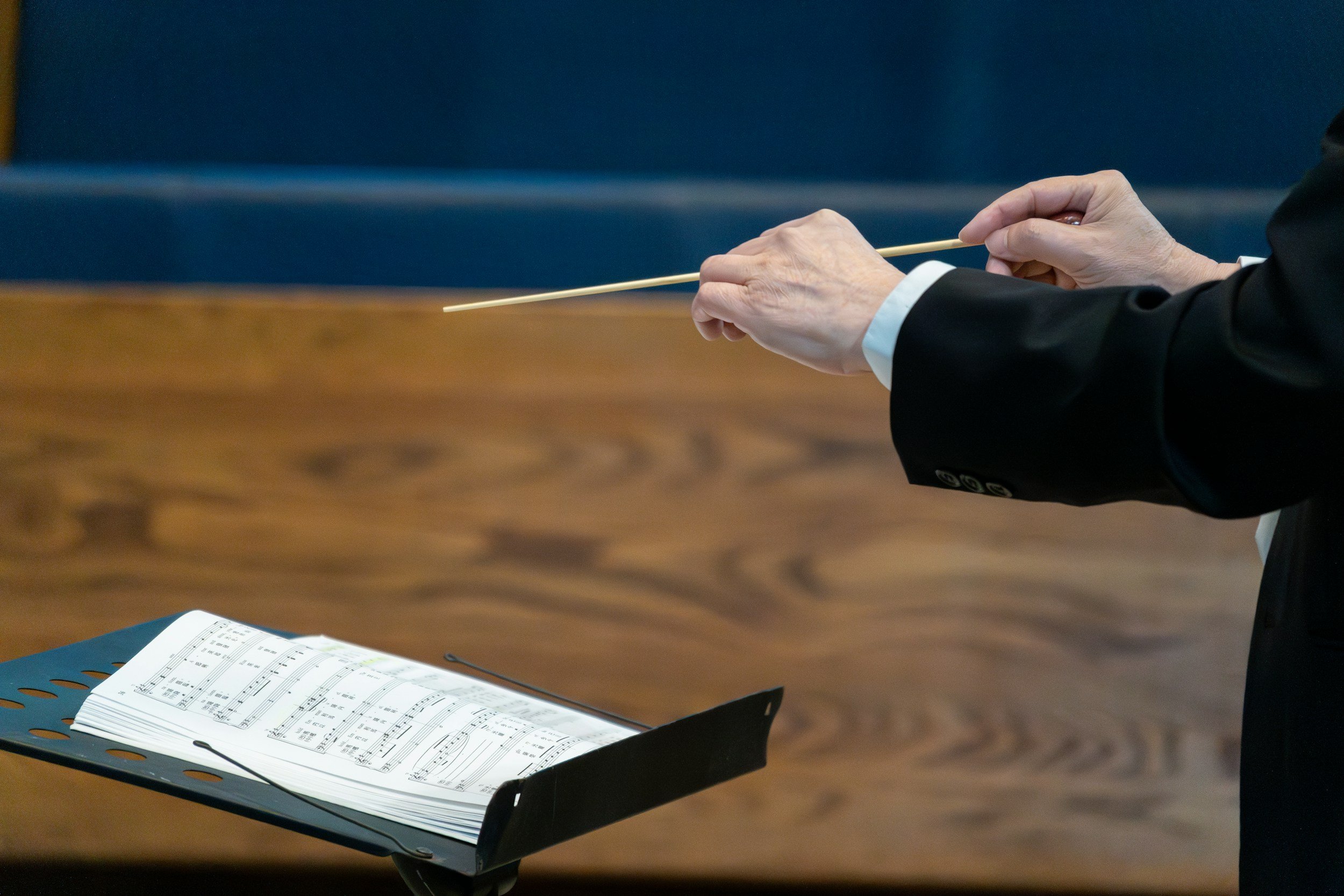 Close-up of a person conducting an orchestra, promoting digital musical education services (including choral part recordings and band part extractions), available nationwide.